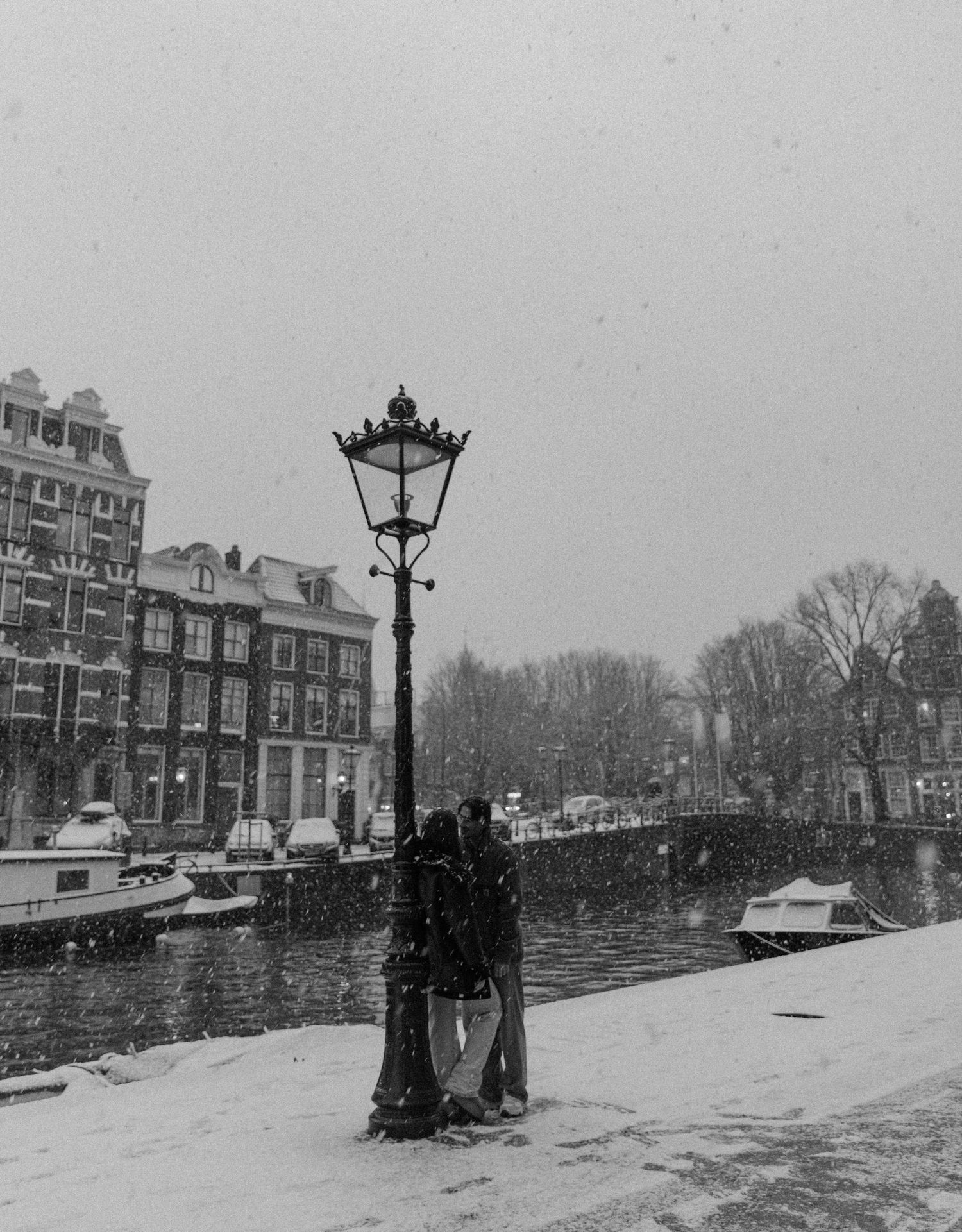 Black and white photograph of snow-covered Amsterdam canal with traditional Dutch buildings.
