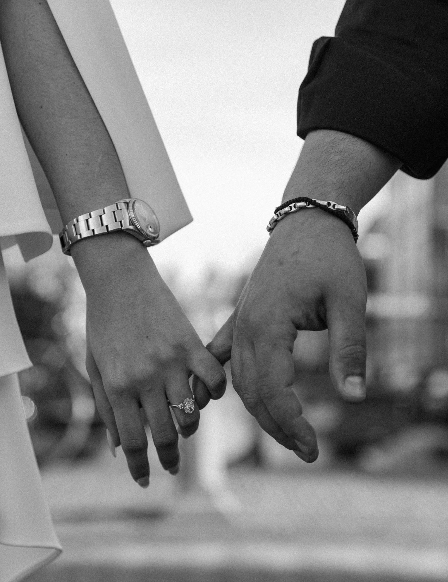 Black and white photo of a couple holding hands, woman wearing engagement ring and watch, man wearing bracelet.