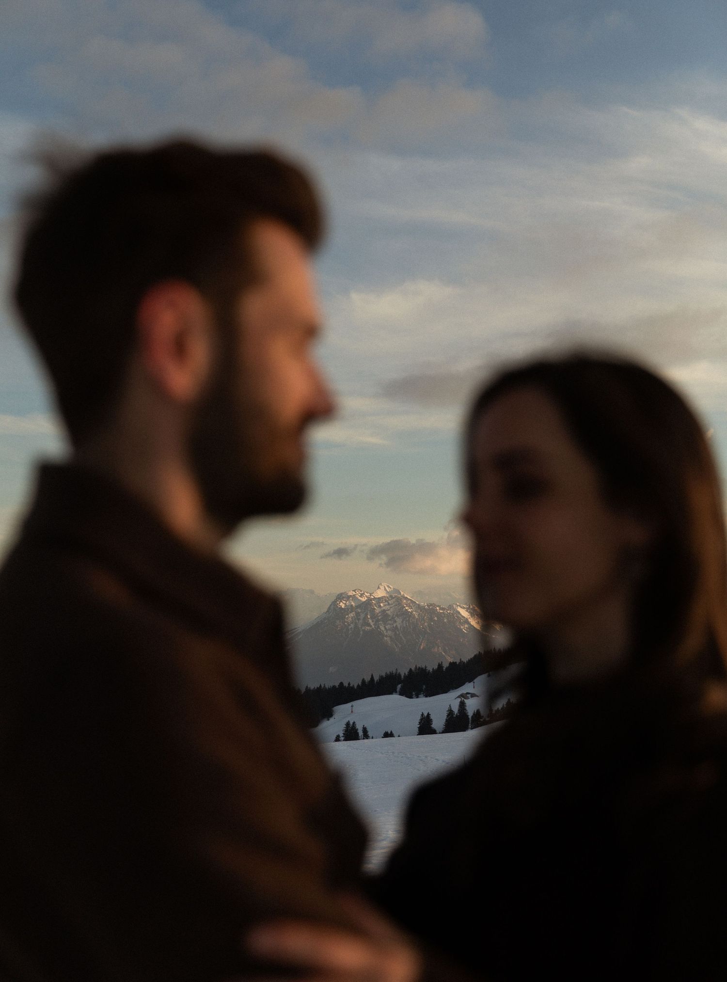 Silhouetted figures stand together against a snowy mountain landscape at sunset.