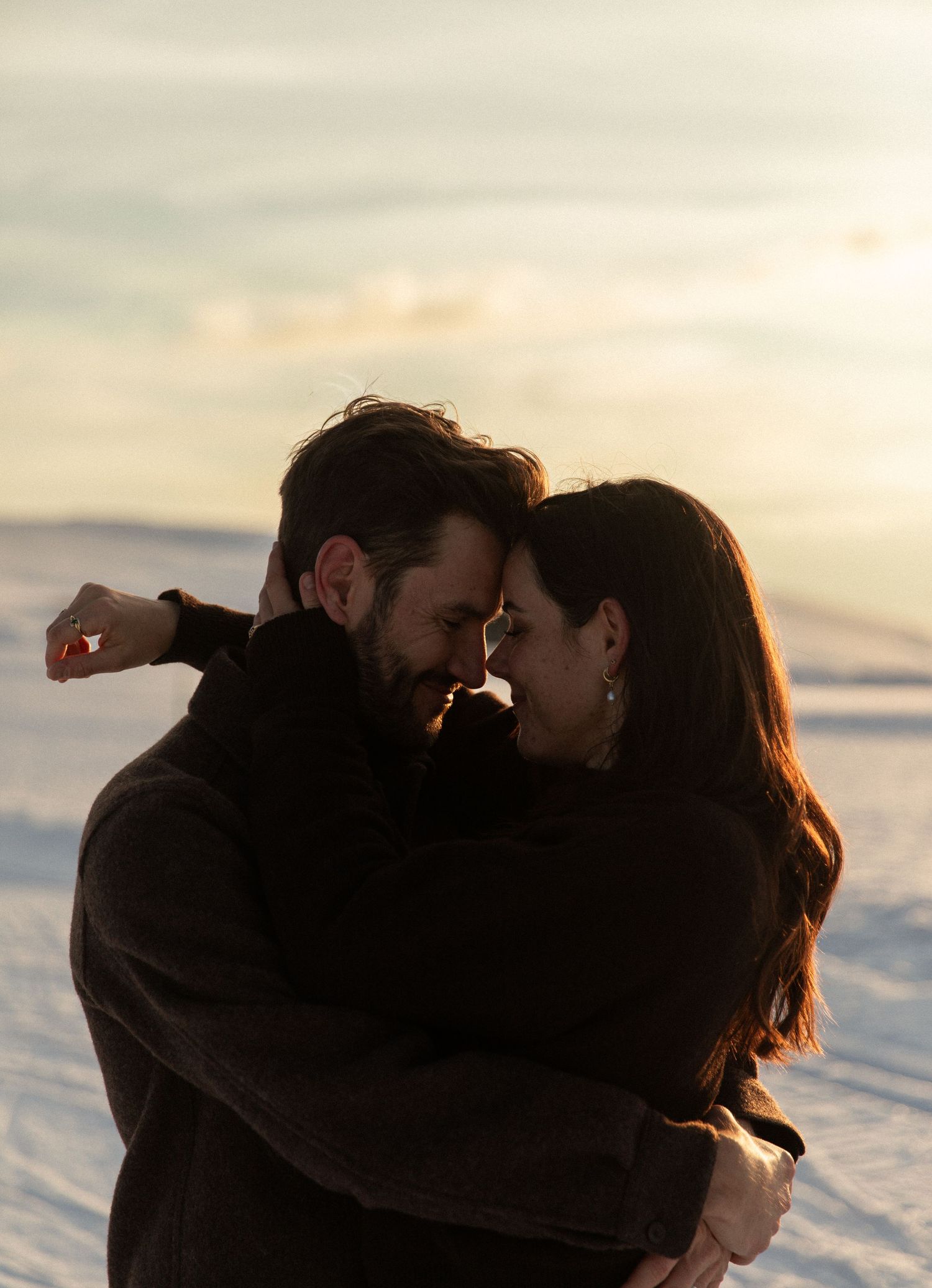 A couple embraces intimately in silhouette against a sunset sky by the water.