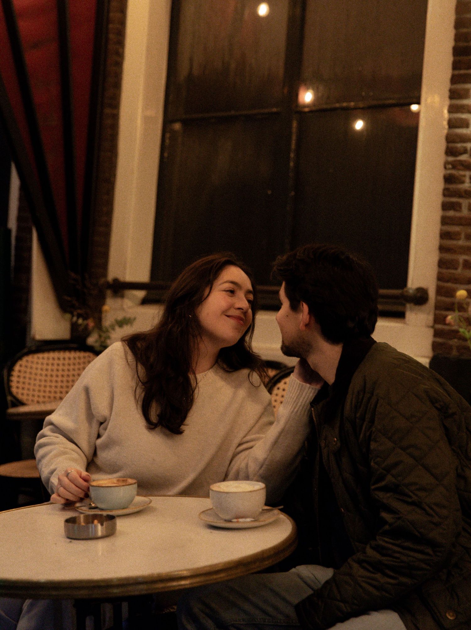An intimate cafe scene with two people sharing coffee and conversation at a small table.