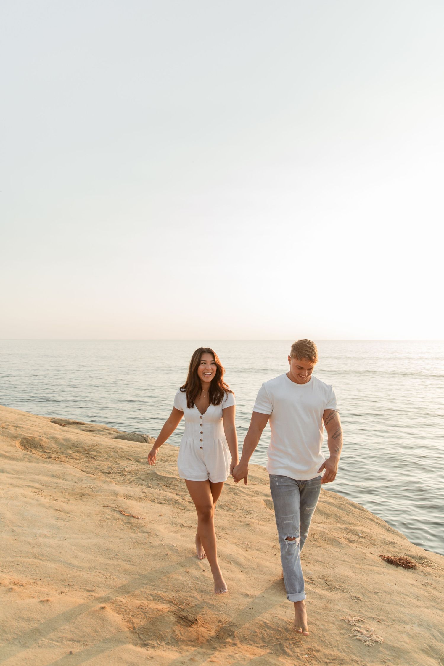 Couple walking hand in hand along a scenic beach at golden hour.