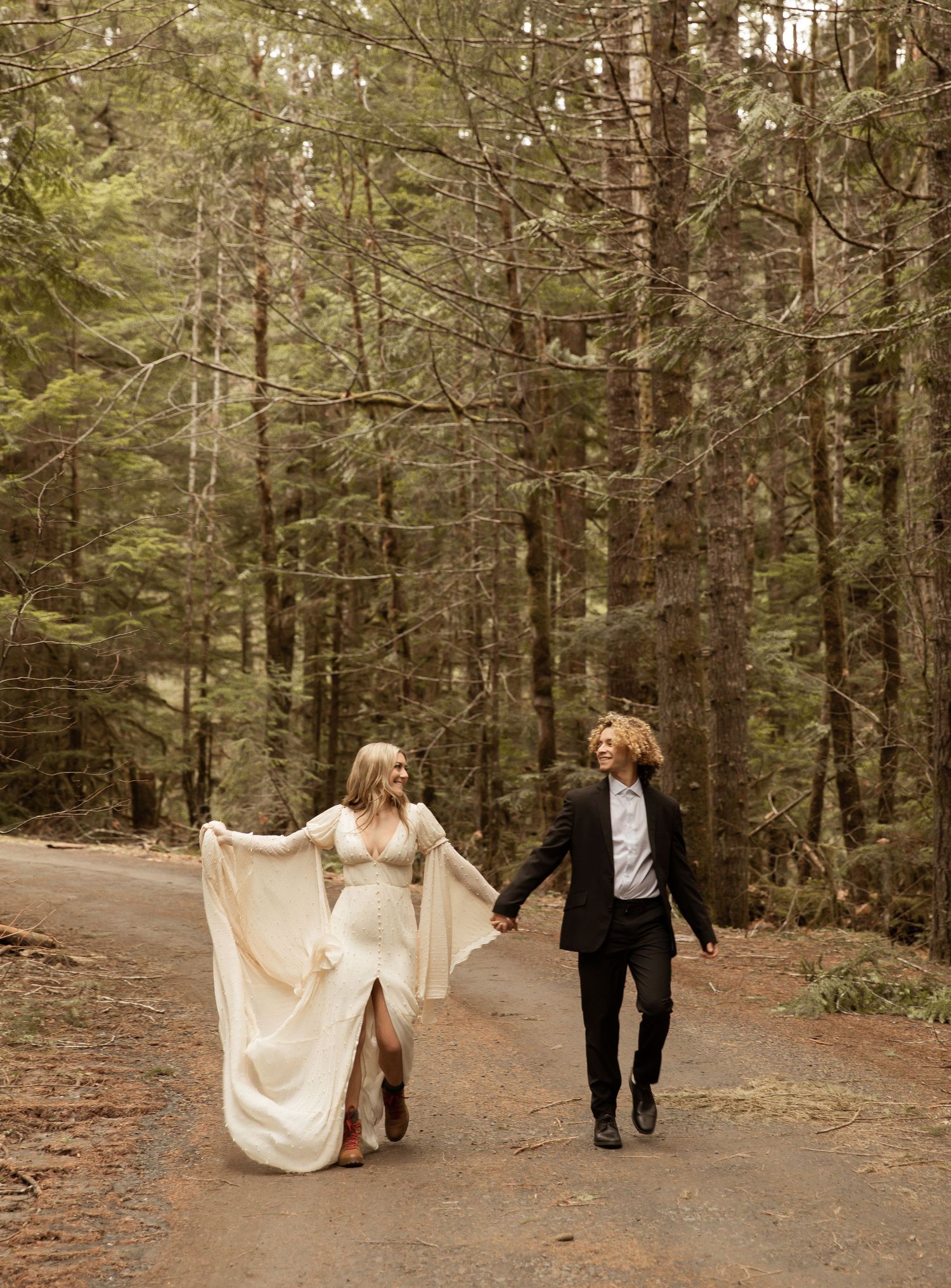 Newlyweds strolling down a pine forest trail with flowing white dress.