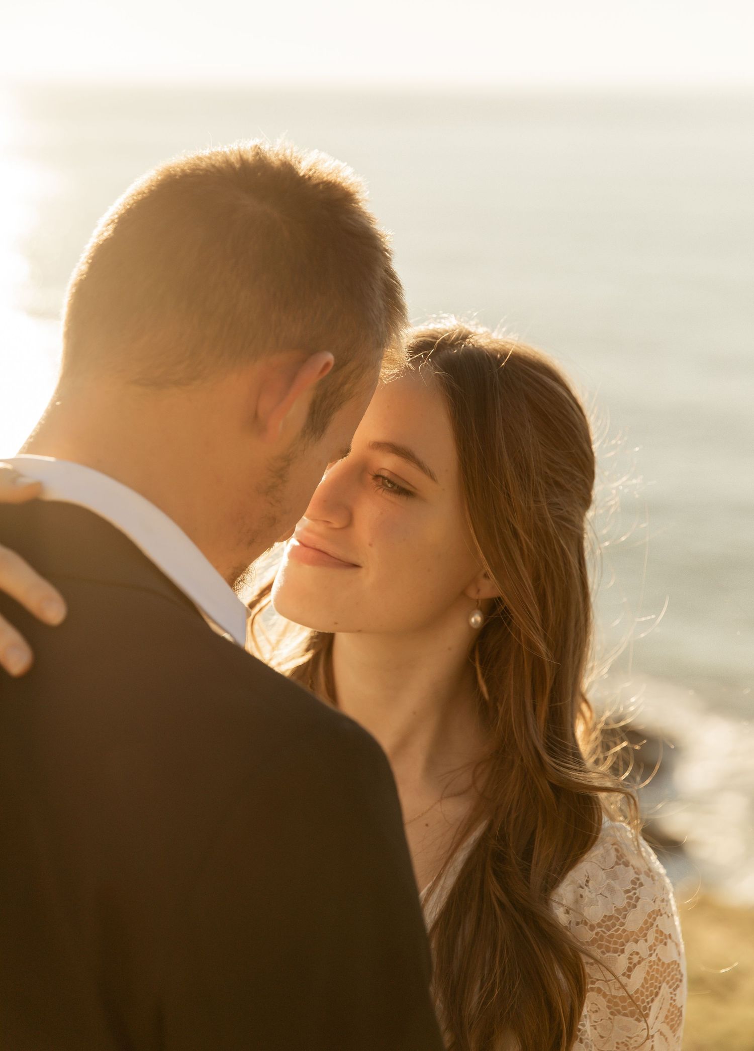 A couple shares a romantic kiss at sunset with golden sunlight creating a dreamy backlit glow.