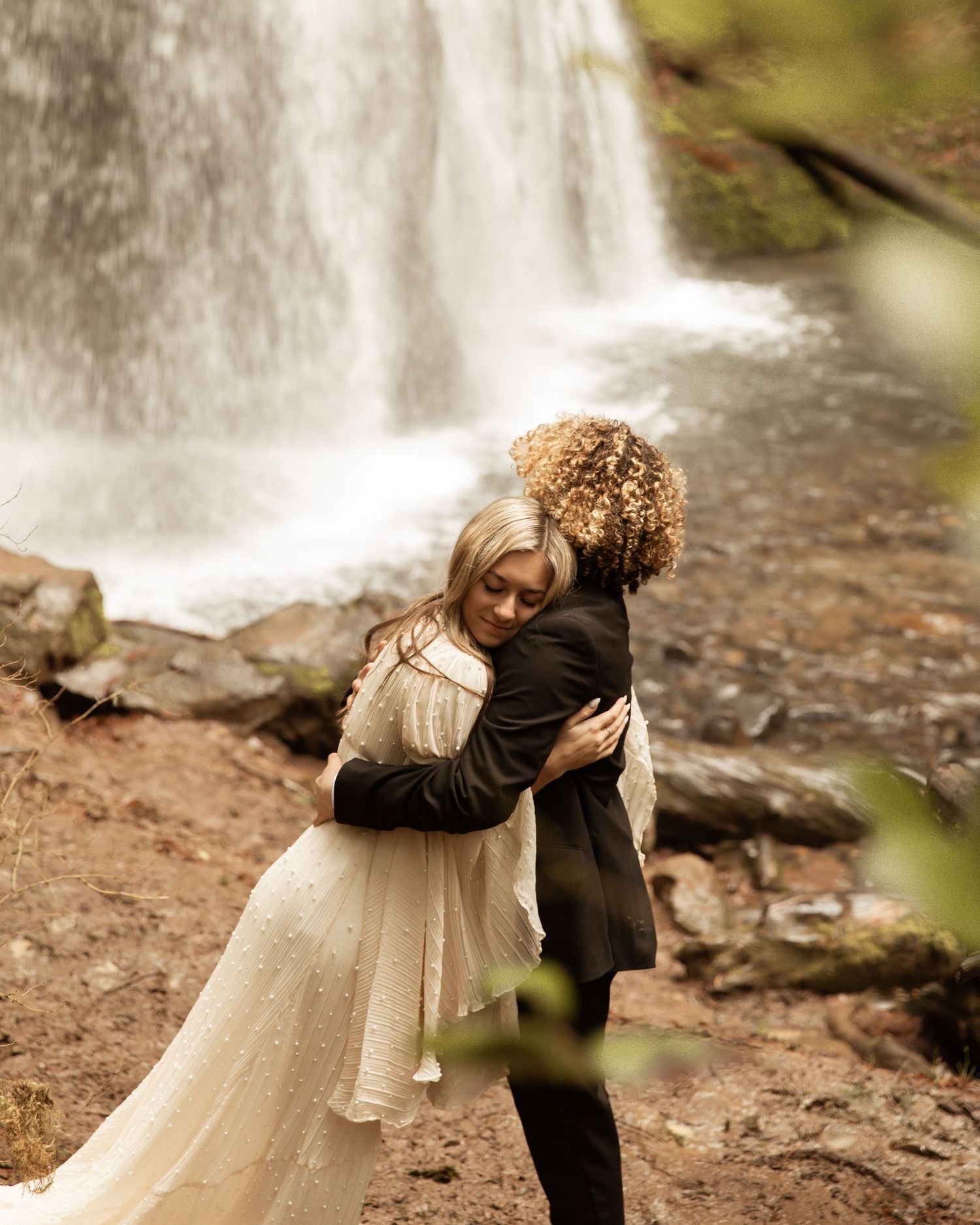 Tender embrace captured against majestic waterfall backdrop in forest setting.
