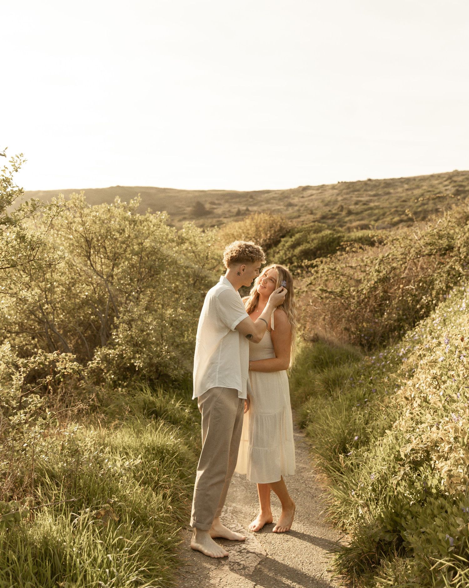 A couple shares an intimate moment on a scenic hillside path during golden hour at sunset.