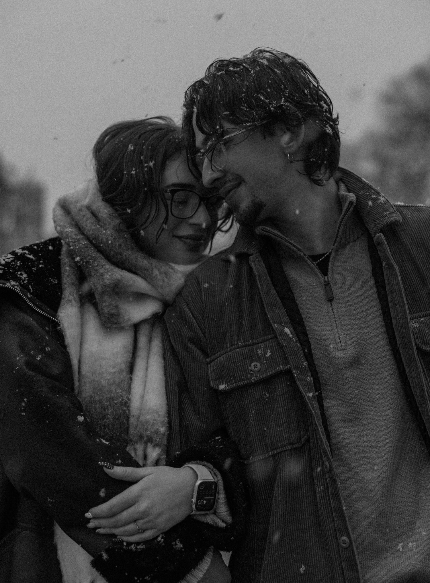 A tender winter moment captured in black and white during snowfall.