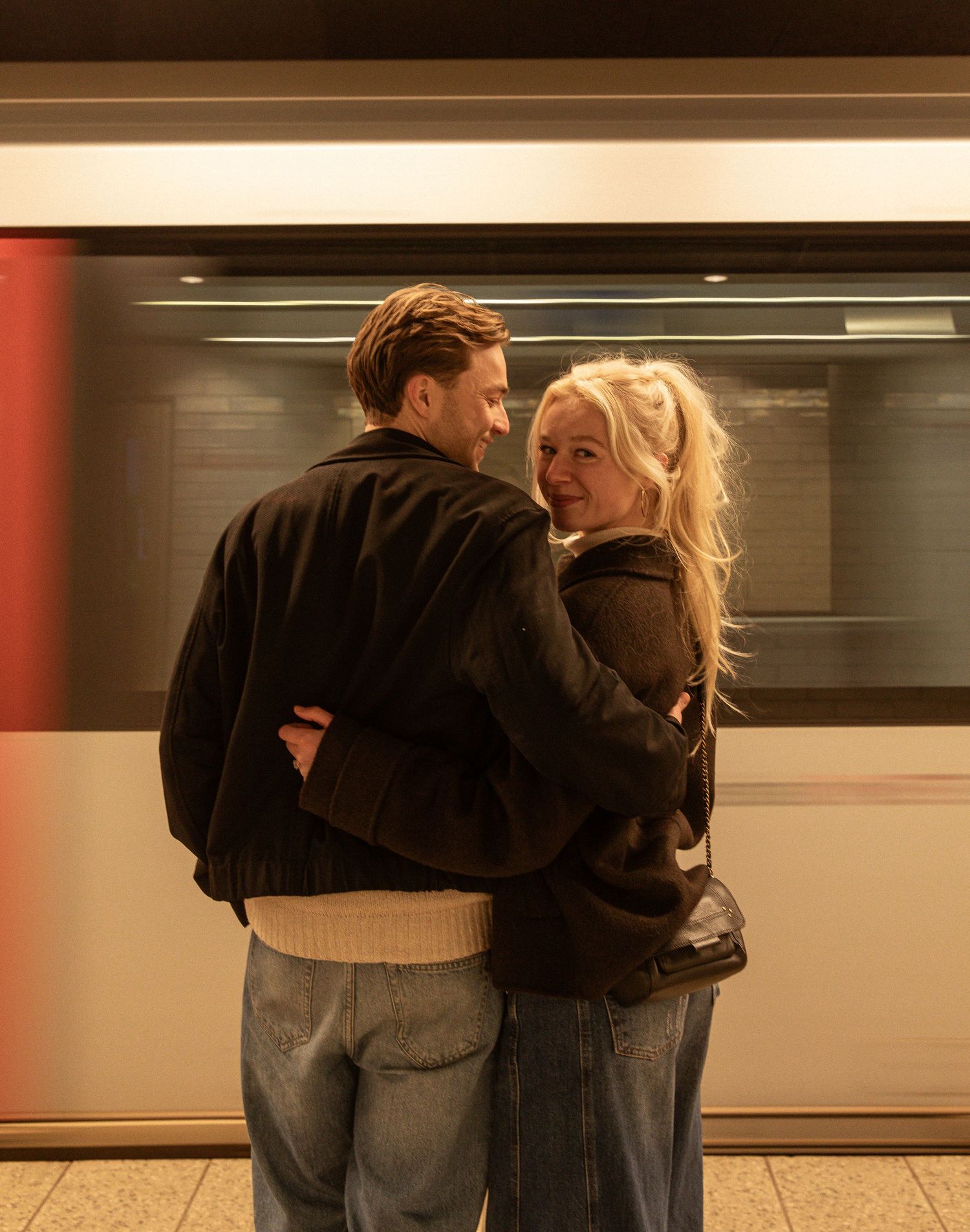 Two people embracing in a dimly lit subway station as a train passes by in the background.