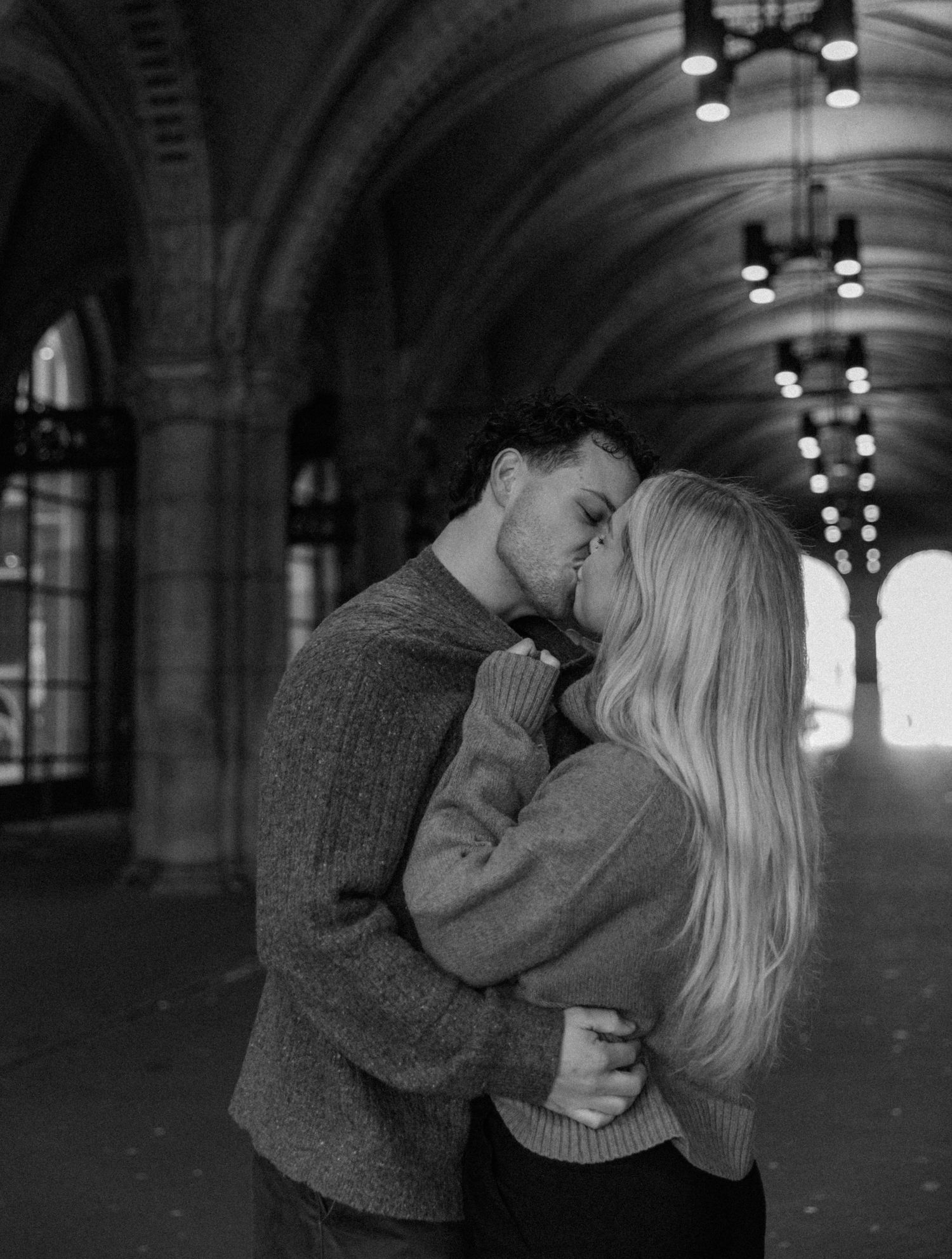 A romantic black and white photo series of a couple sharing intimate moments under an arched tunnel with dramatic lighting.