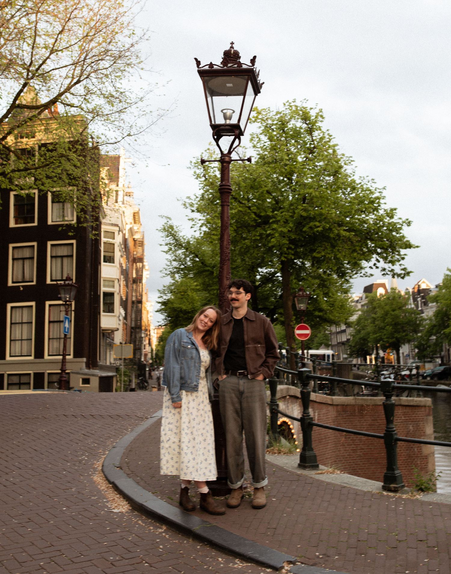 A couple poses under a vintage street lamp on a brick canal corner in Amsterdam, Netherlands.