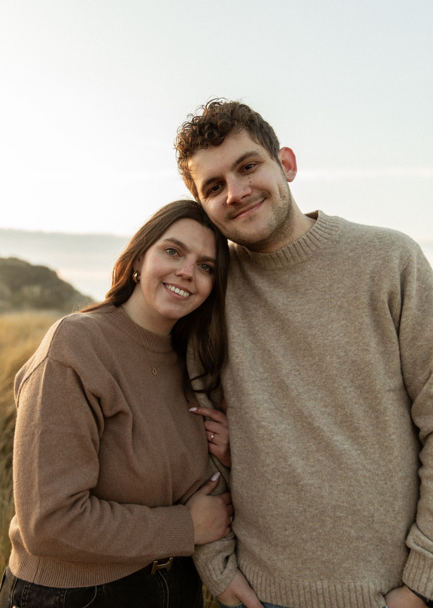 Couple in cozy sweaters embracing outdoors during golden hour.