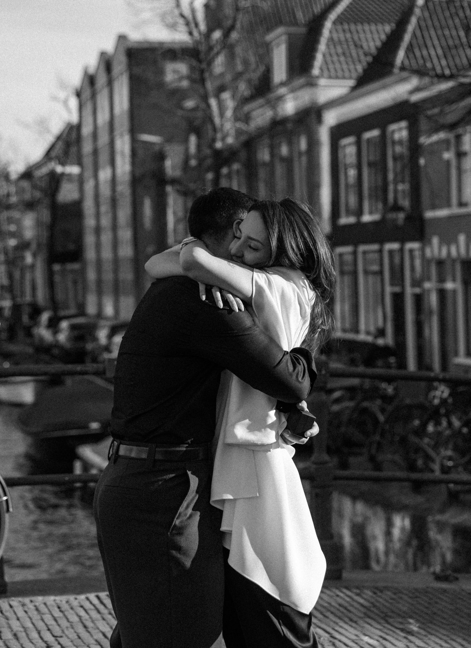 Black and white photo of a couple embracing tenderly on a canal bridge in Amsterdam.