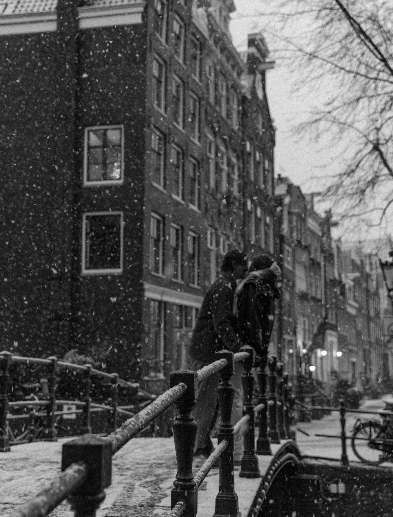 Snow covered streets of Amsterdam with traditional Dutch architecture and bare trees.