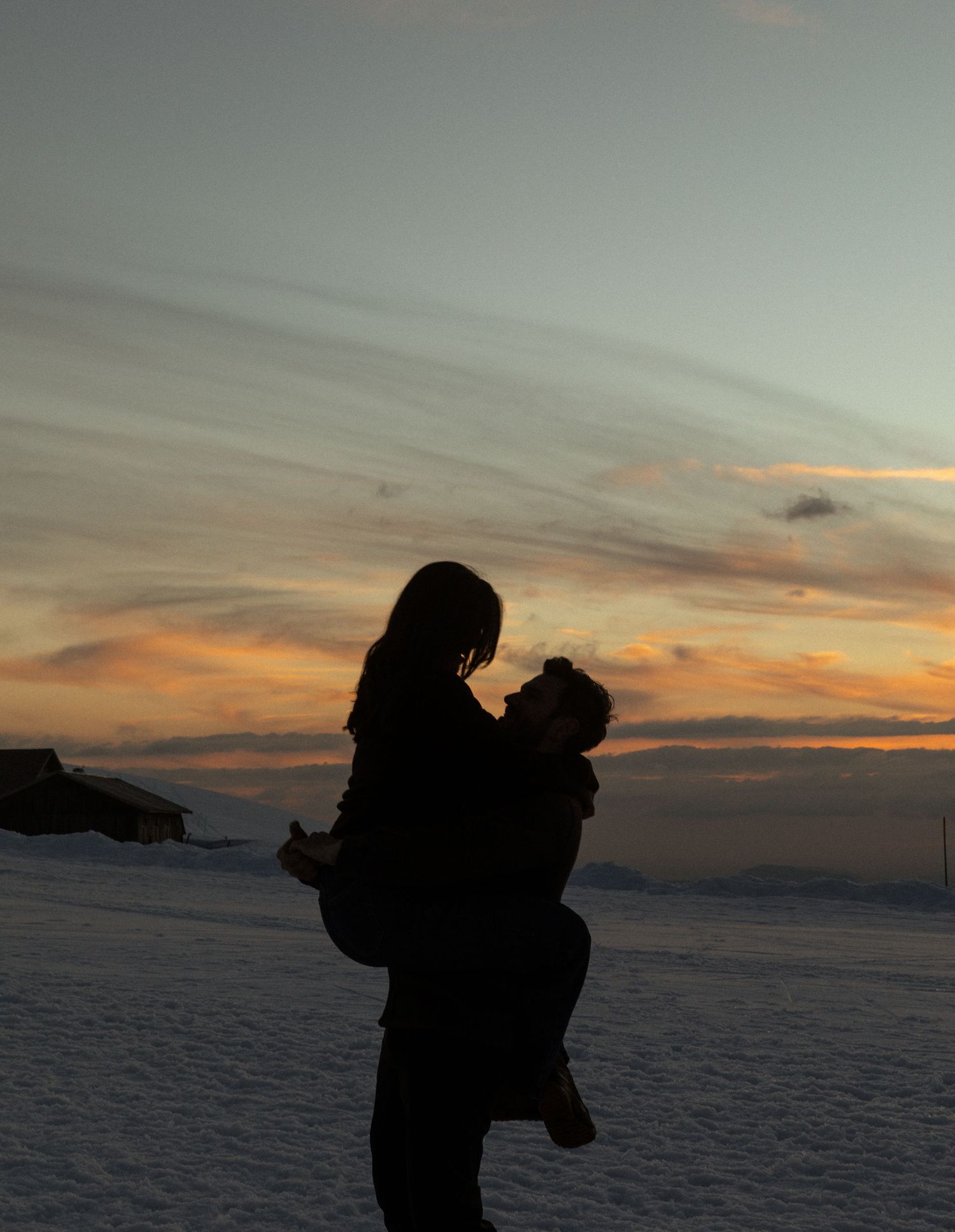 Silhouettes of people walking across a snowy landscape against a dramatic sunset sky with orange and purple hues.