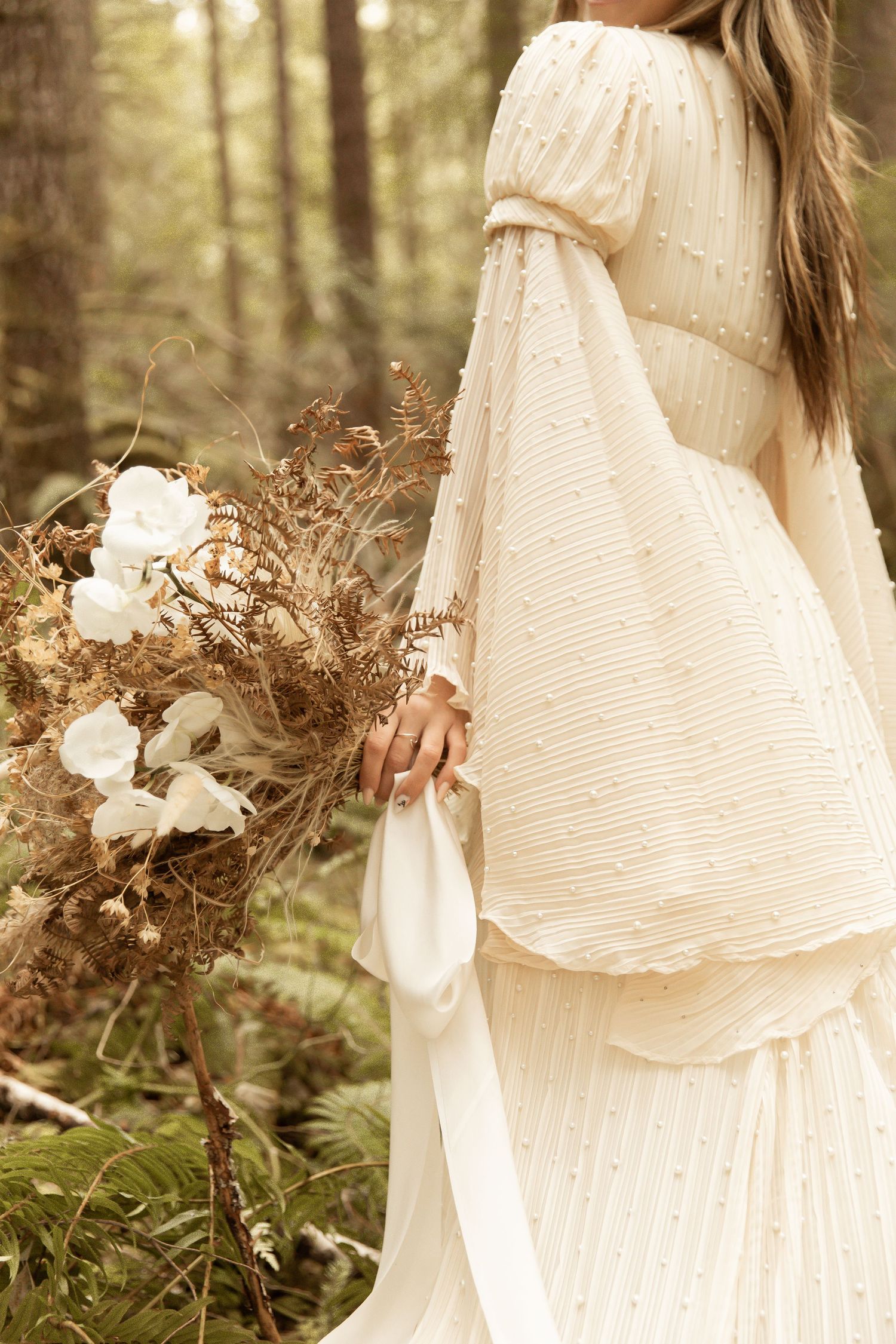 Ethereal white dress flowing in a mystical forest setting with dried flowers and natural elements.