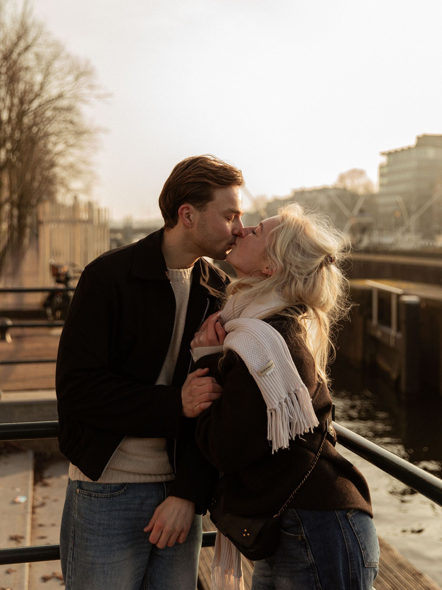 Romantic couple sharing an intimate moment on a bridge during sunset in an urban setting.