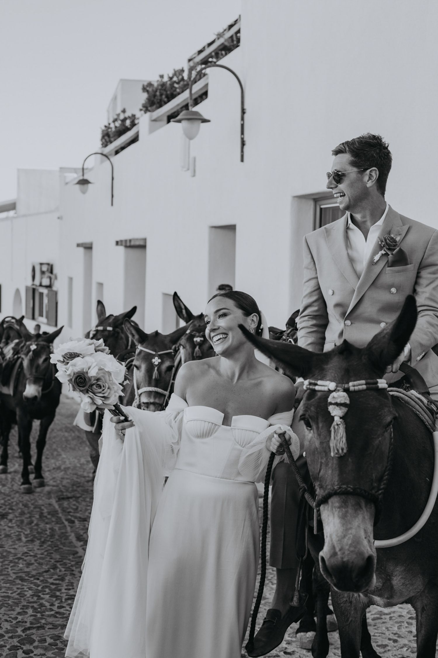A joyful wedding couple laughs while interacting with a horse in Santorini