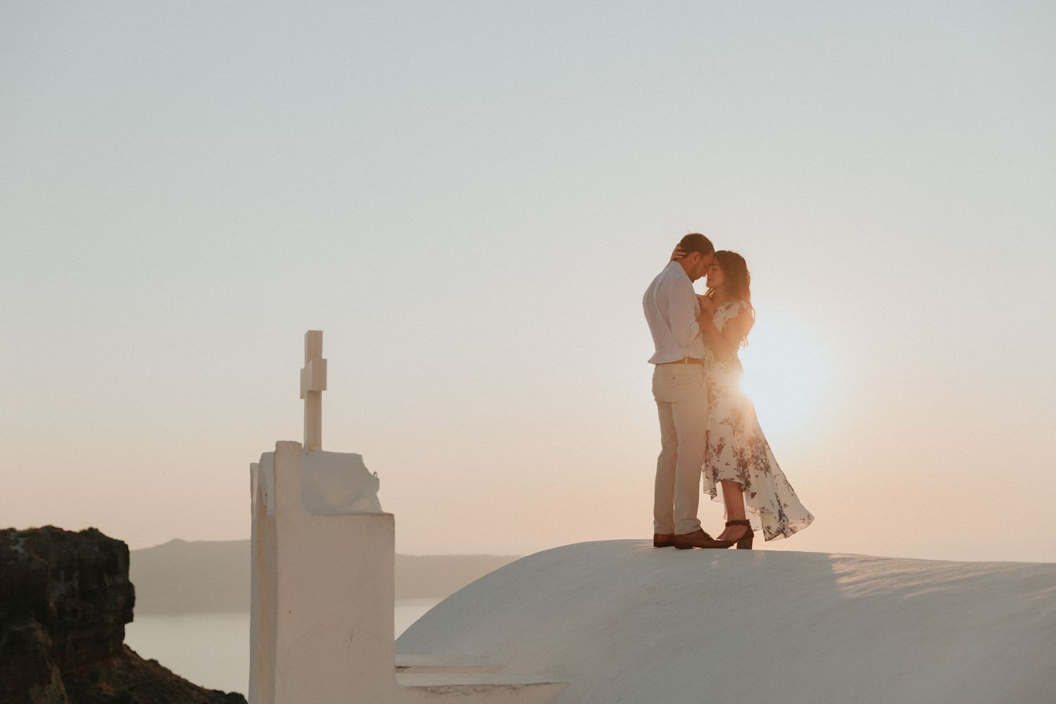 Couple embracing on a church rooftop in Santorini, Greece at sunset