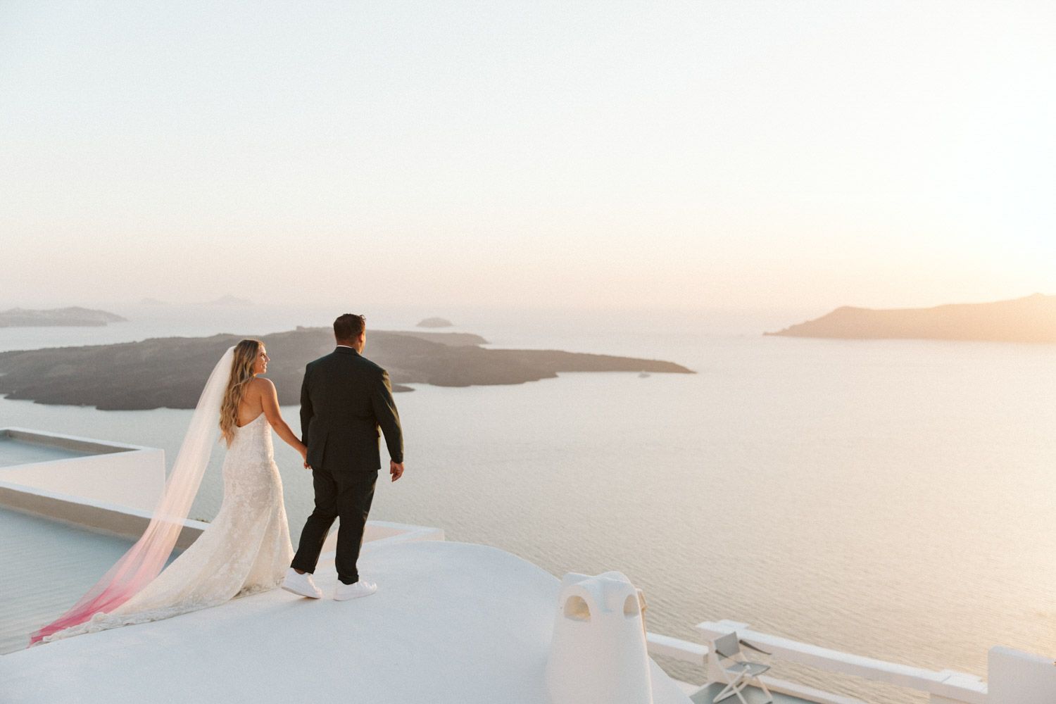 Wedding couple walking on a rooftop Santorini, Greece towards the sunset