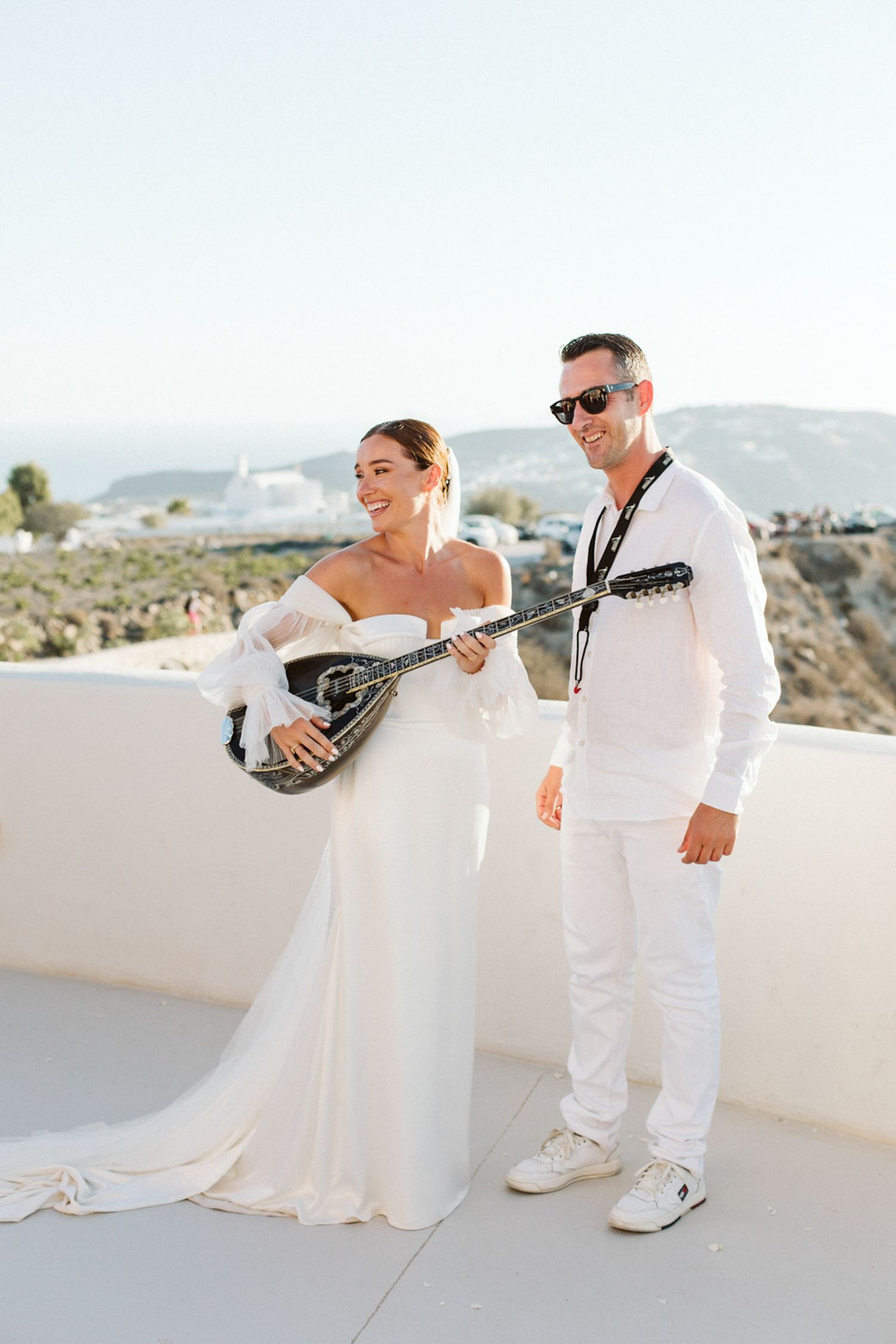 A bride holding a bouzouki against a scenic backdrop in Santorini