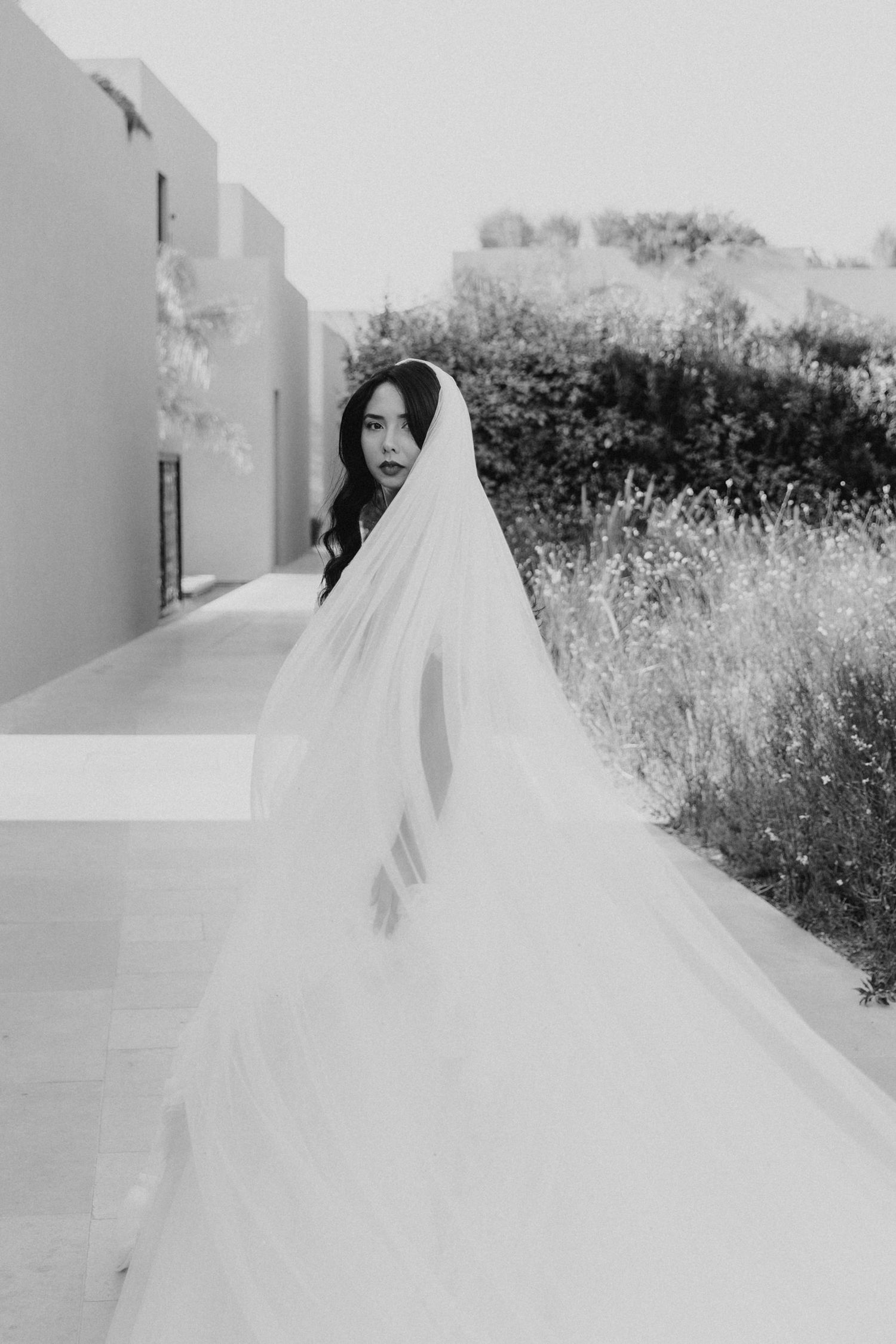A black and white photo showing a bride in a flowing white dress on her wedding day in Samos, Greece