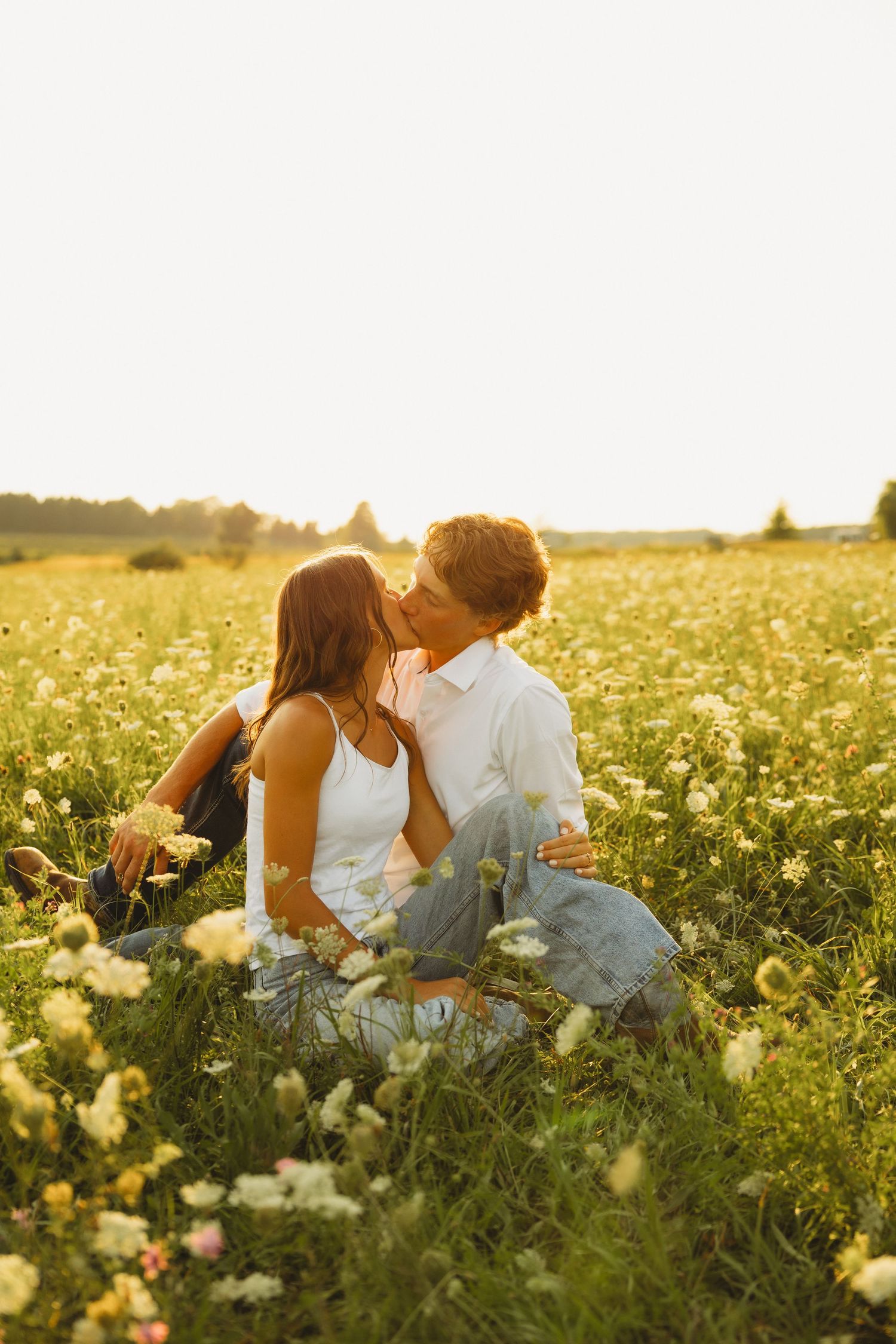 Couple kissing while sitting in a sunny wildflower meadow at golden hour.