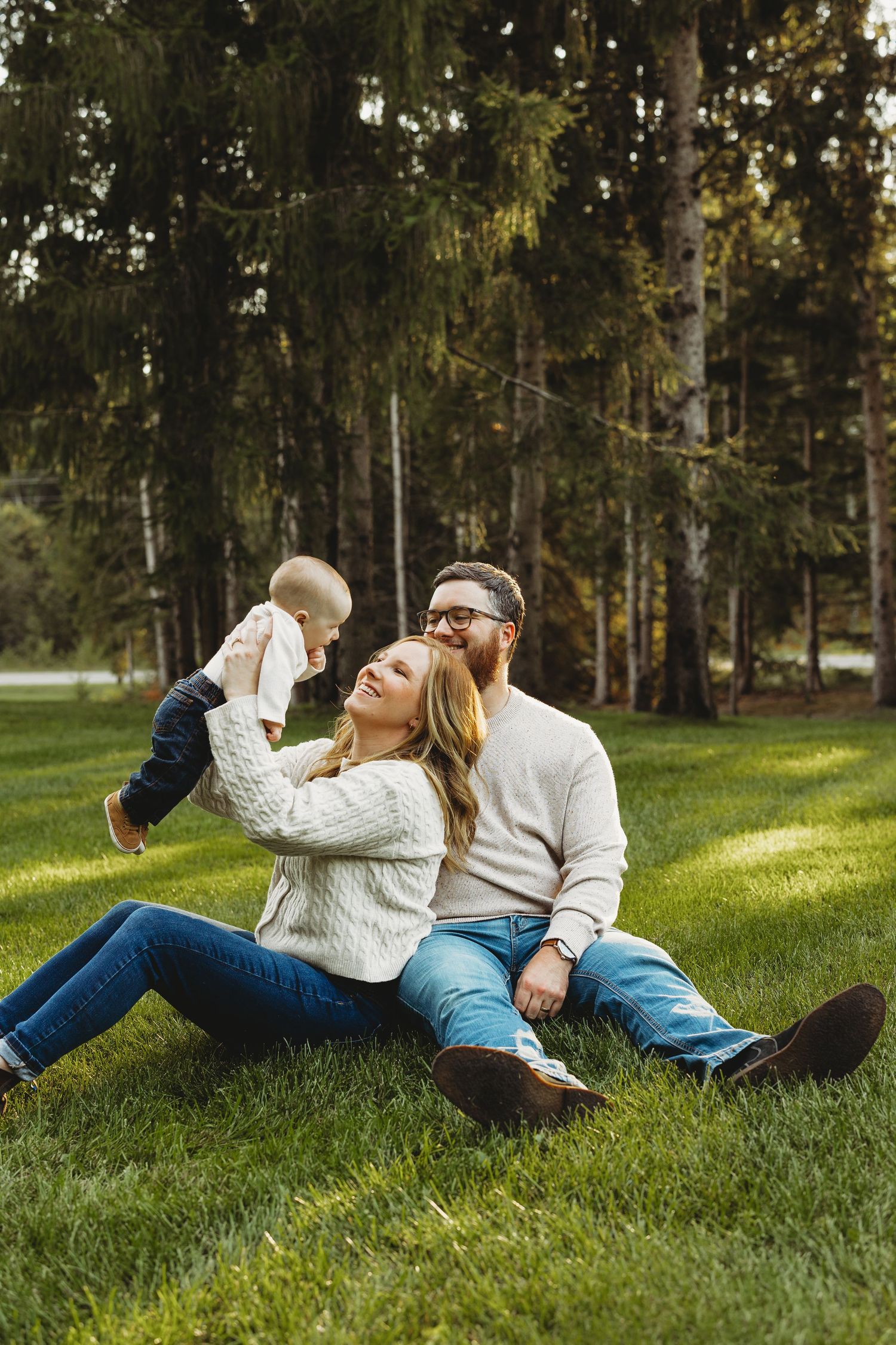 Family lying together on green grass during golden hour in a park setting.