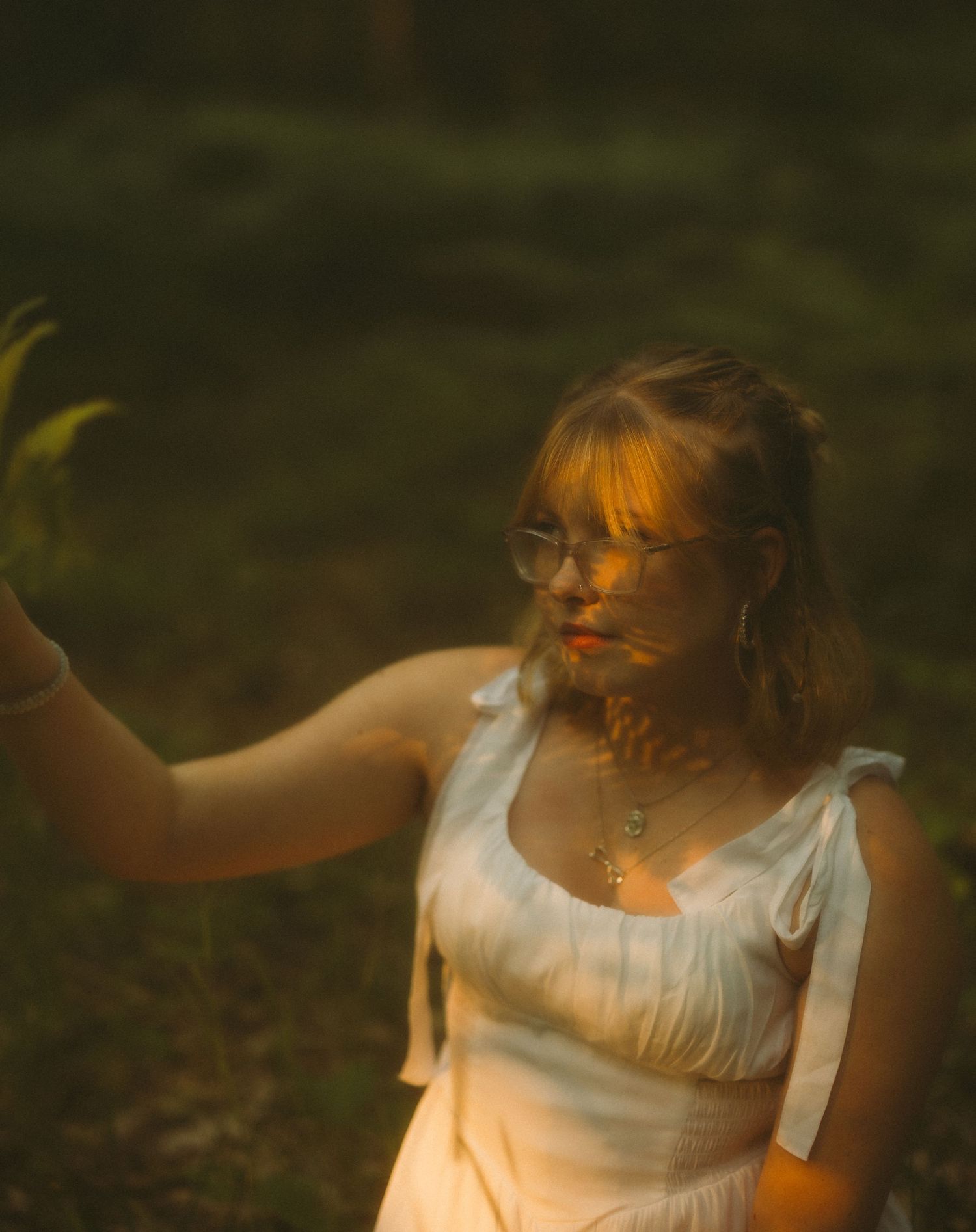 Person in white dress illuminated by warm sunset light in natural outdoor setting.