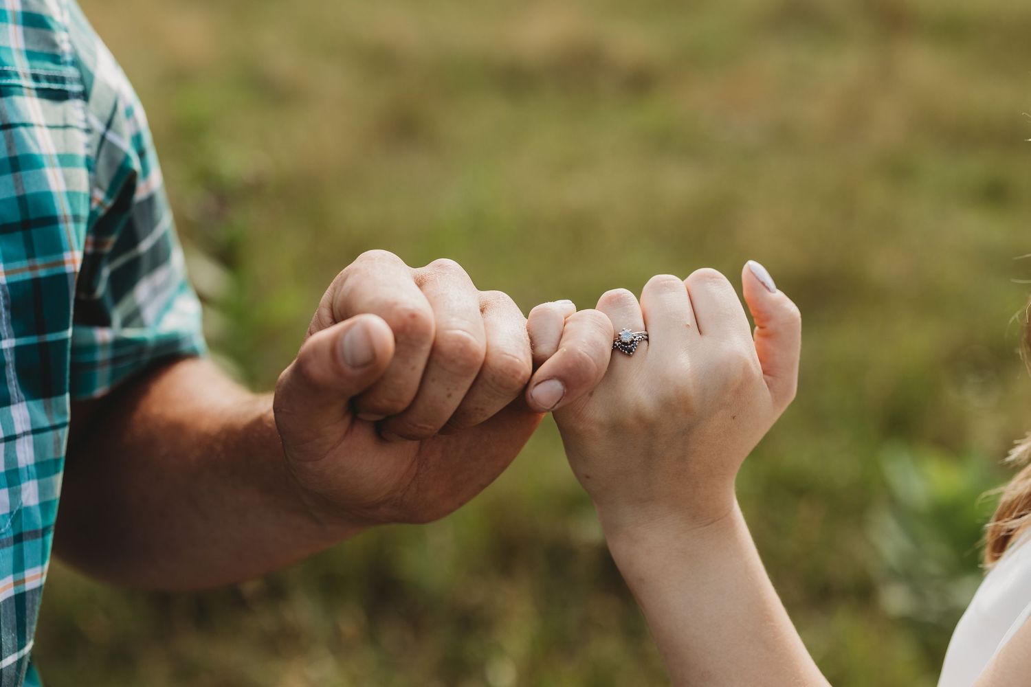 Two people pinky swear with their hands against a blurred green outdoor background.
