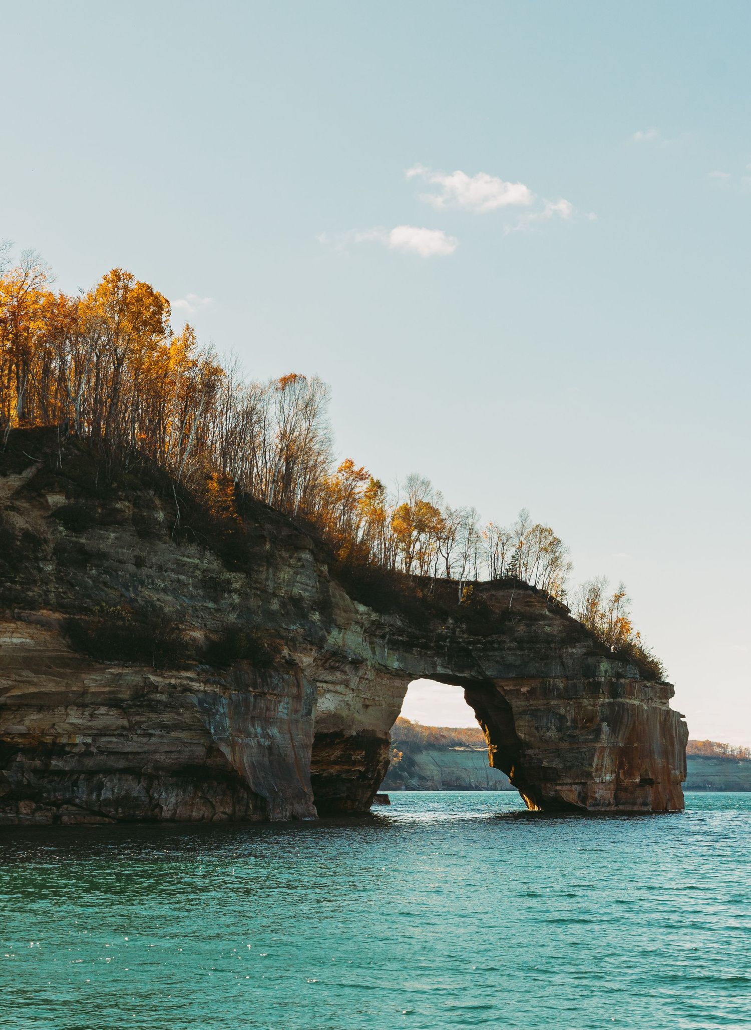 Natural stone arch formation in Pictured Rocks National Lakeshore with fall foliage along the cliff top.
