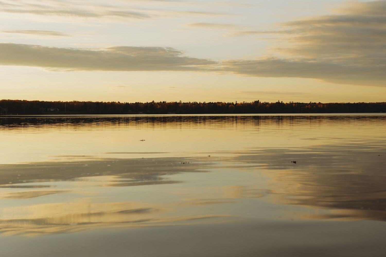 Serene panoramic view of sunset clouds reflecting on still lake waters.