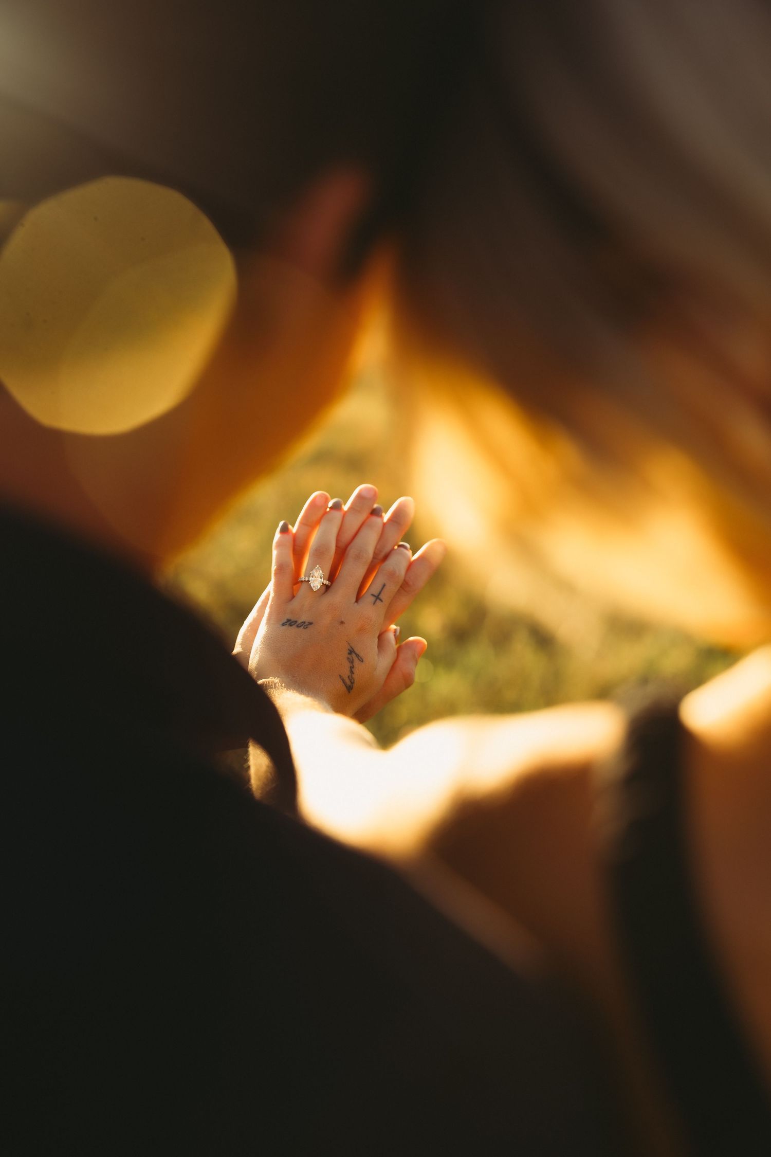 Person with hands pressed together in prayer, doodle drawings inked on their fingers, softly lit by golden sunlight over blurred grass.