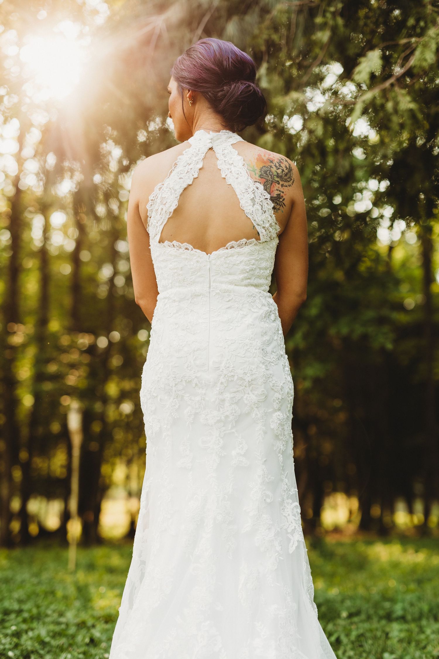 Elegant white lace wedding dress with keyhole back detail shown in a sunlit outdoor garden setting.