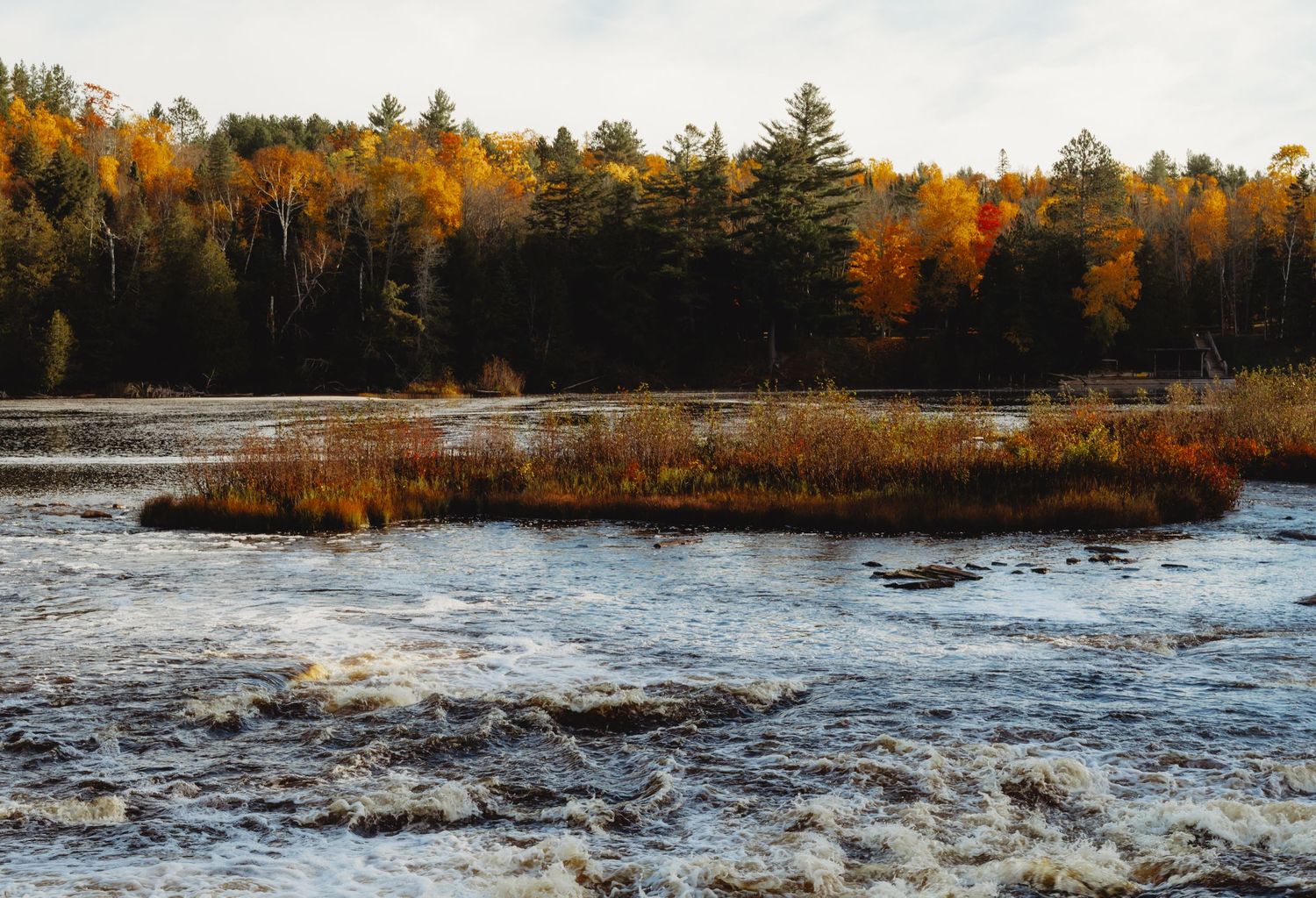 Panoramic autumn landscape of a rocky river with rushing water and colorful fall foliage along the banks.
