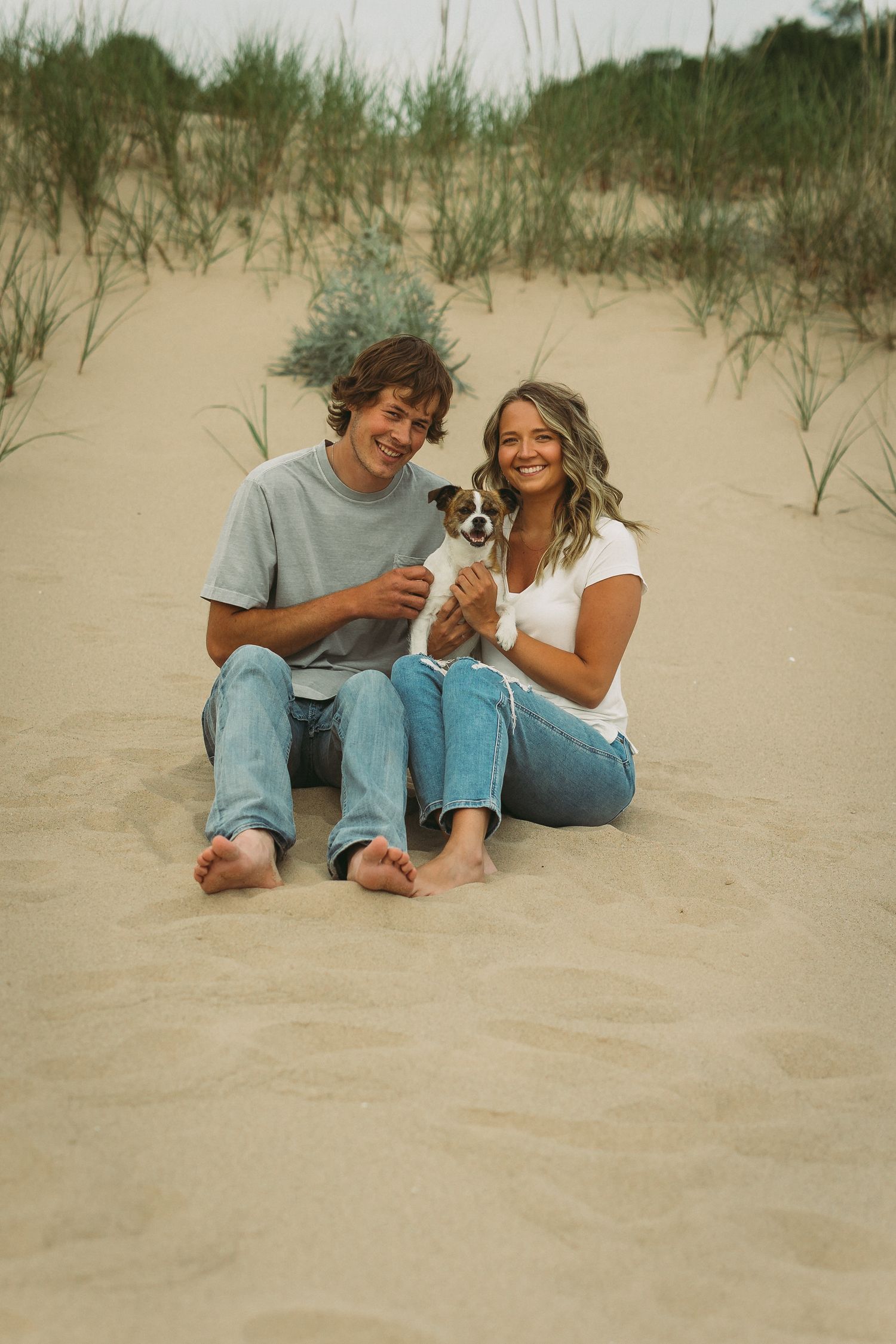 Two people relaxing and laughing together on sandy dunes with beach grass.