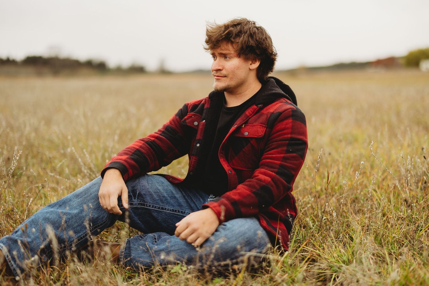 Person relaxing in grassy field wearing red plaid flannel and jeans.