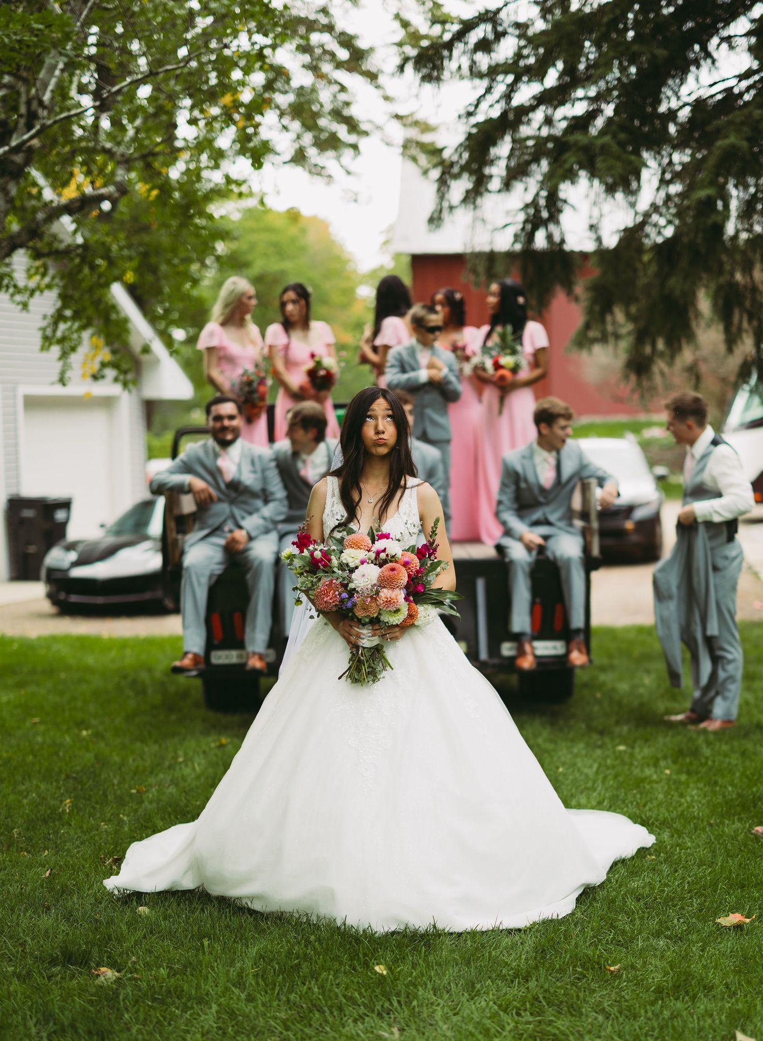 Wedding party gathers on a lush green lawn with bridesmaids in pink and groomsmen in gray.