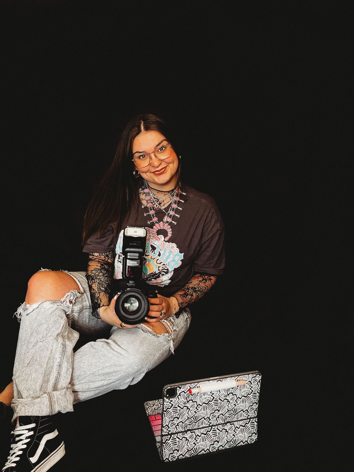 A photographer with camera equipment poses against a black background.