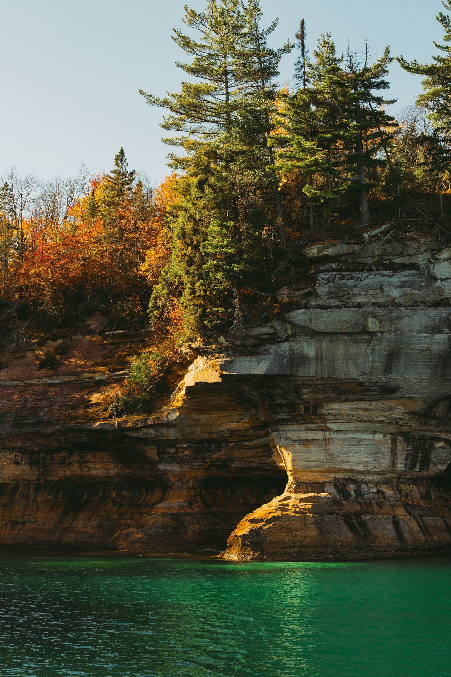 Rugged limestone cliffs with evergreen trees reflected in emerald green waters below.