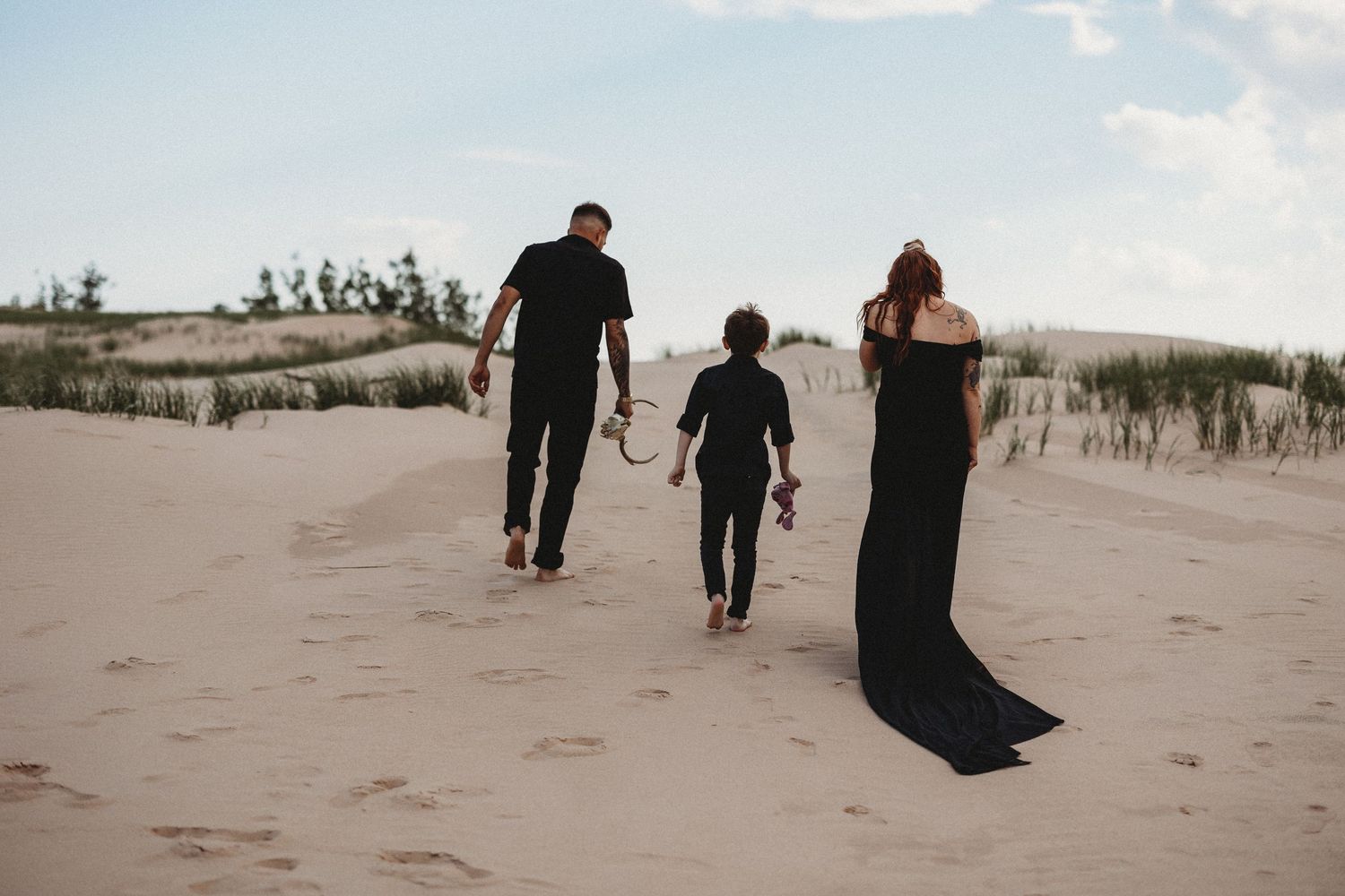 A group of people walking along a sandy beach path with dunes and grass in the background.