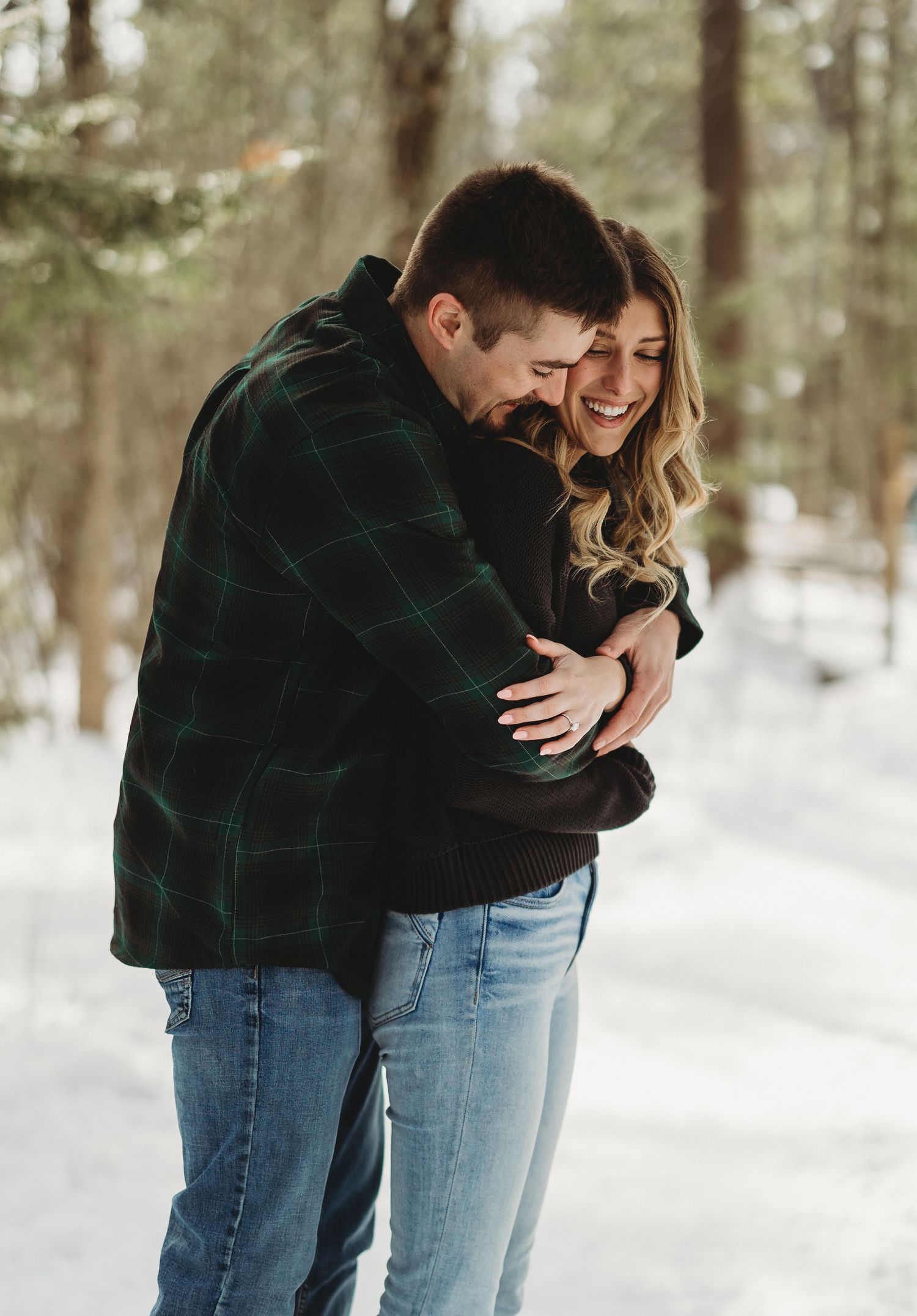 Winter engagement photos showing a couple embracing in a snowy forest setting.