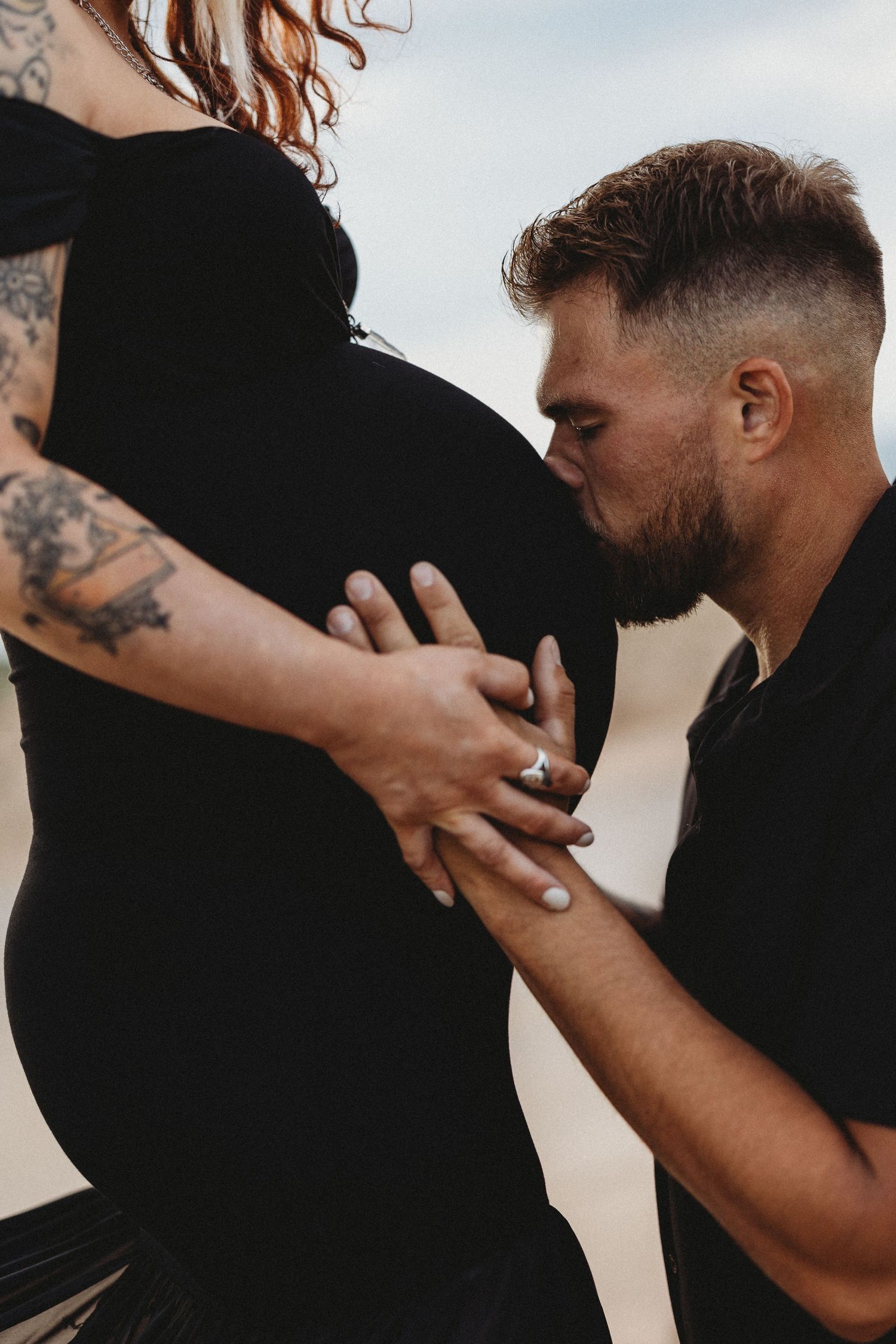 Intimate maternity portrait of couple in black clothing on beach.