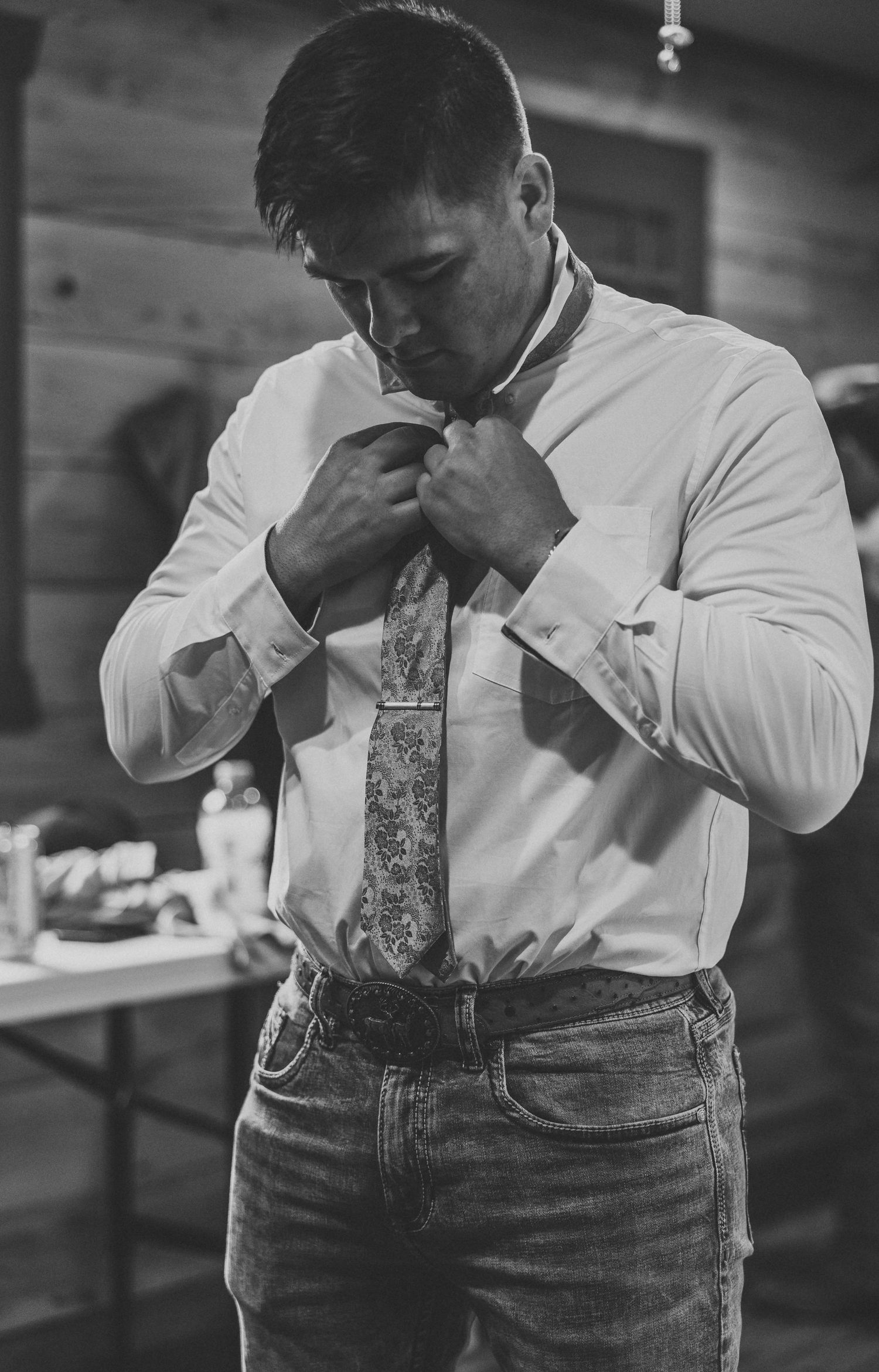Black and white photo of someone adjusting a floral tie while getting dressed.