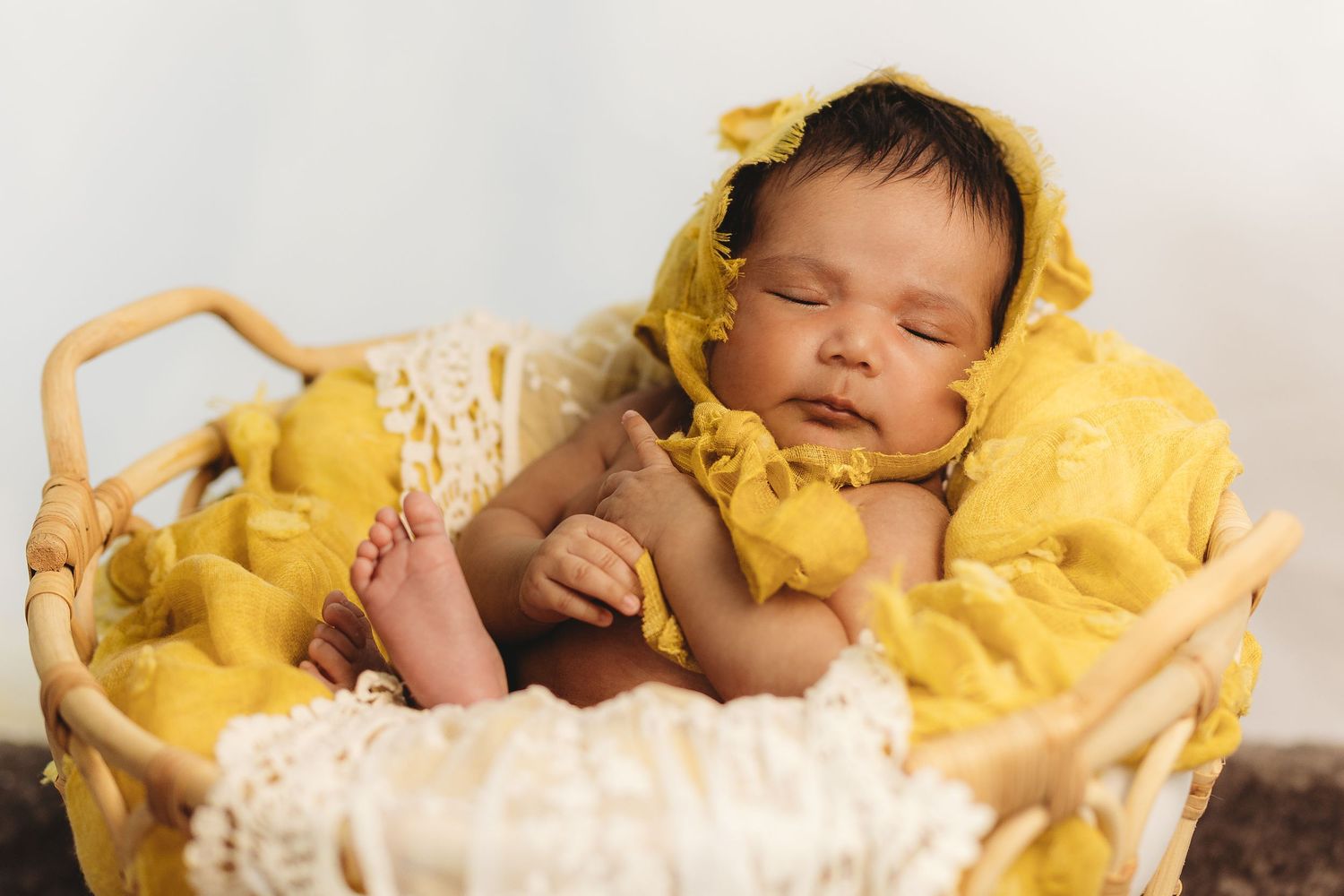 Sleeping newborn nestled in soft yellow blanket during photo session.