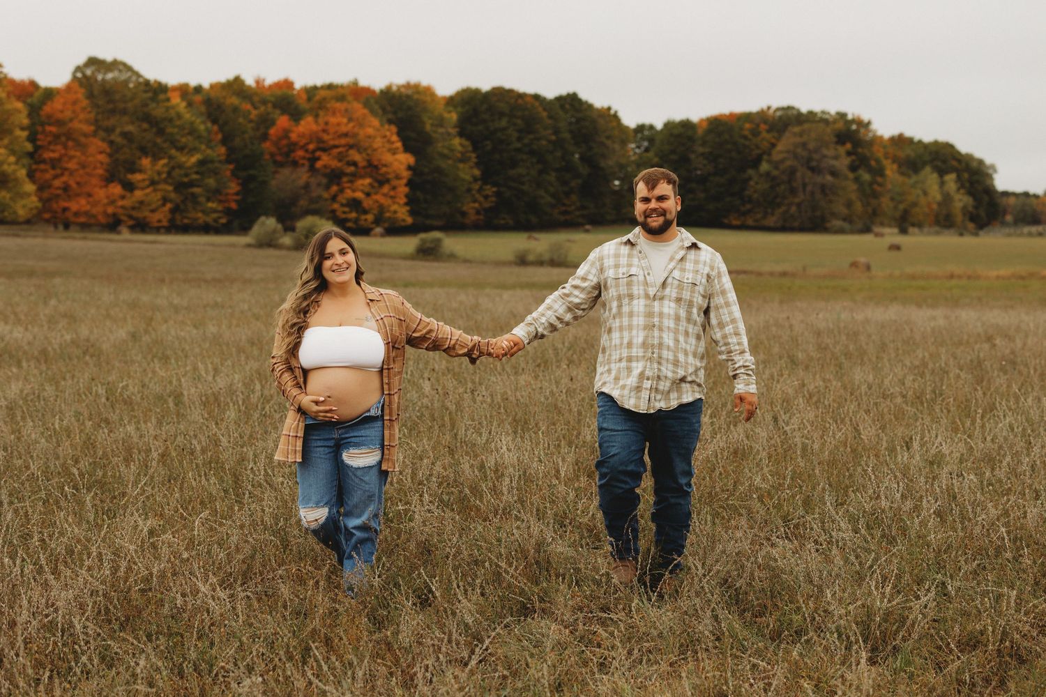 Couple walking hand in hand through a golden autumn field during sunset.