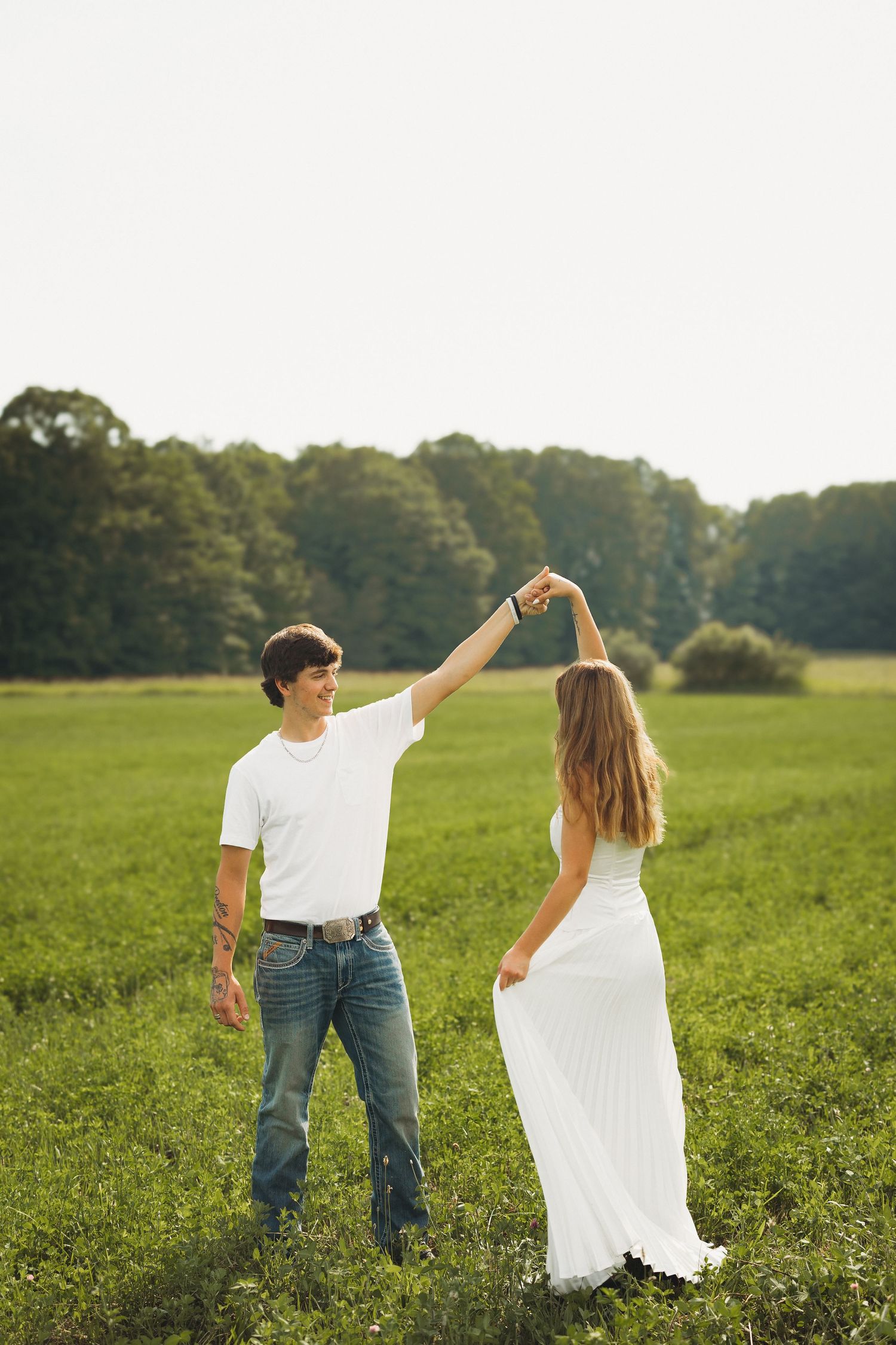 Couple dancing in a green field, man in white tee and jeans twirling woman in flowing white dress.