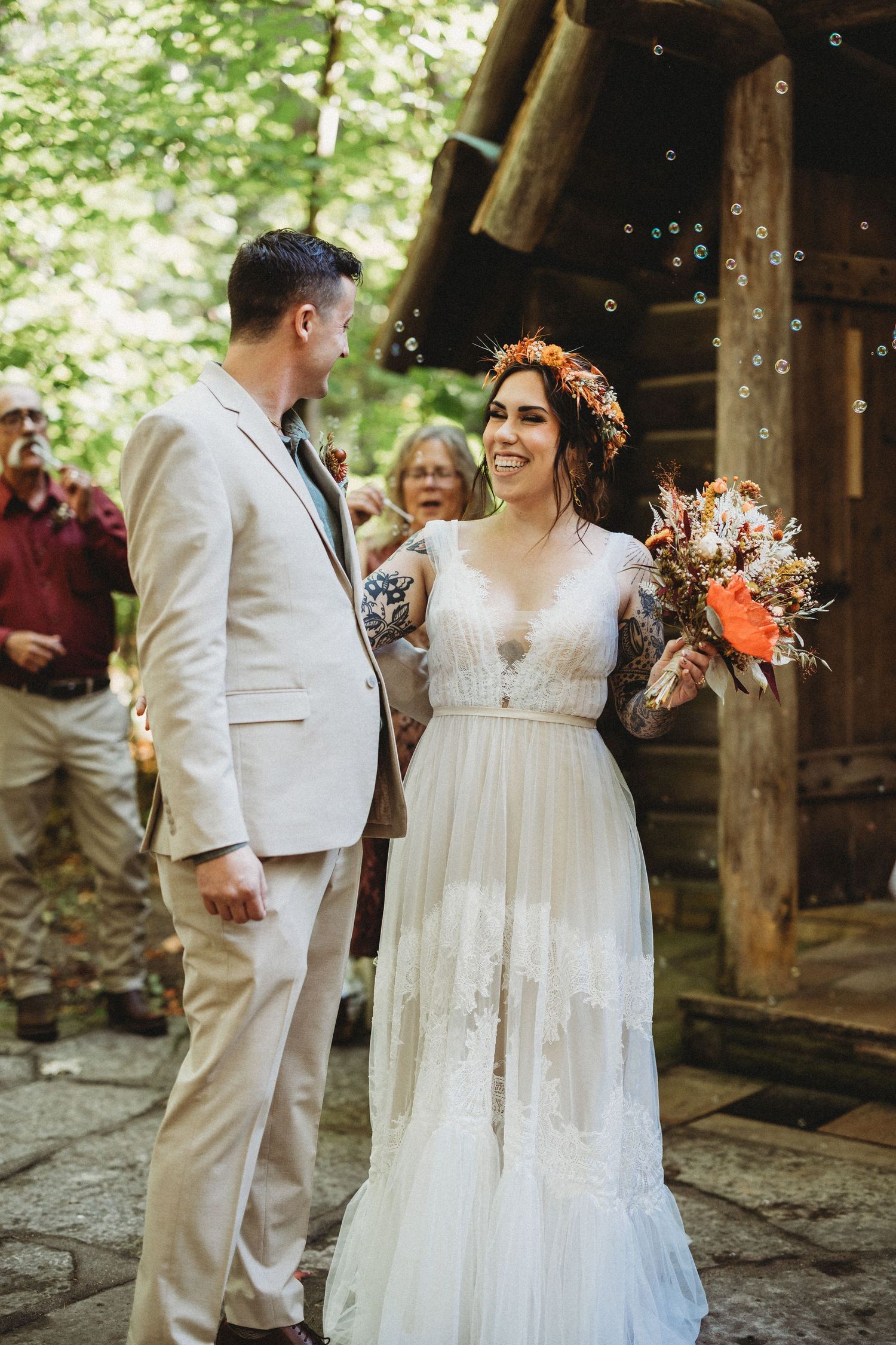A couple shares joyful moments in an outdoor wedding setting with natural greenery and rustic wooden elements.