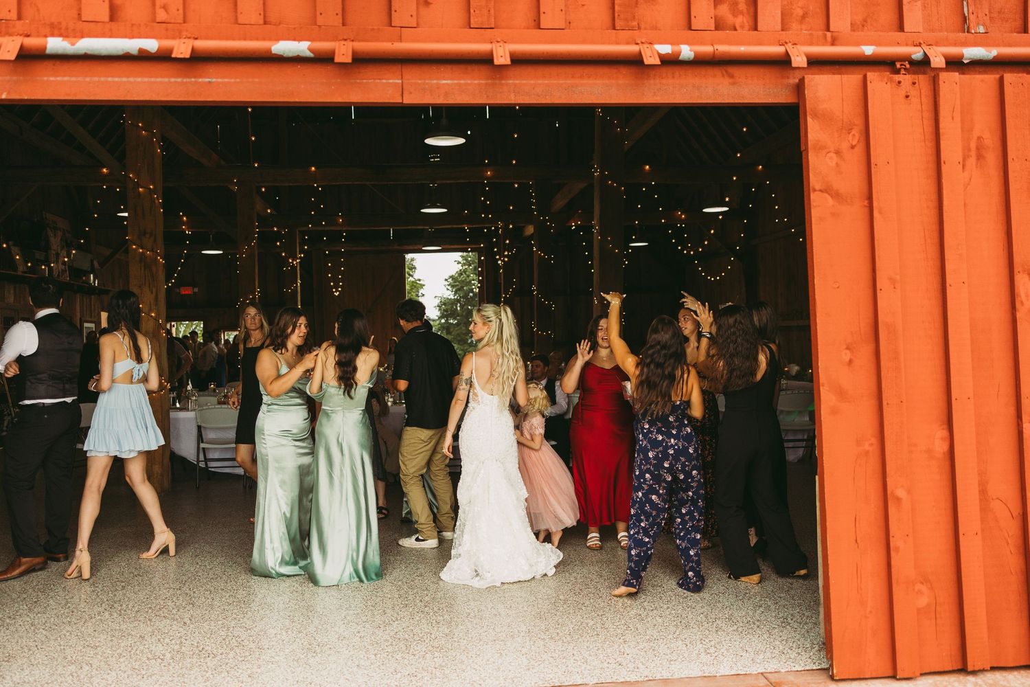 A group of people dancing at a formal event on a wooden dance floor with orange curtains in the background.