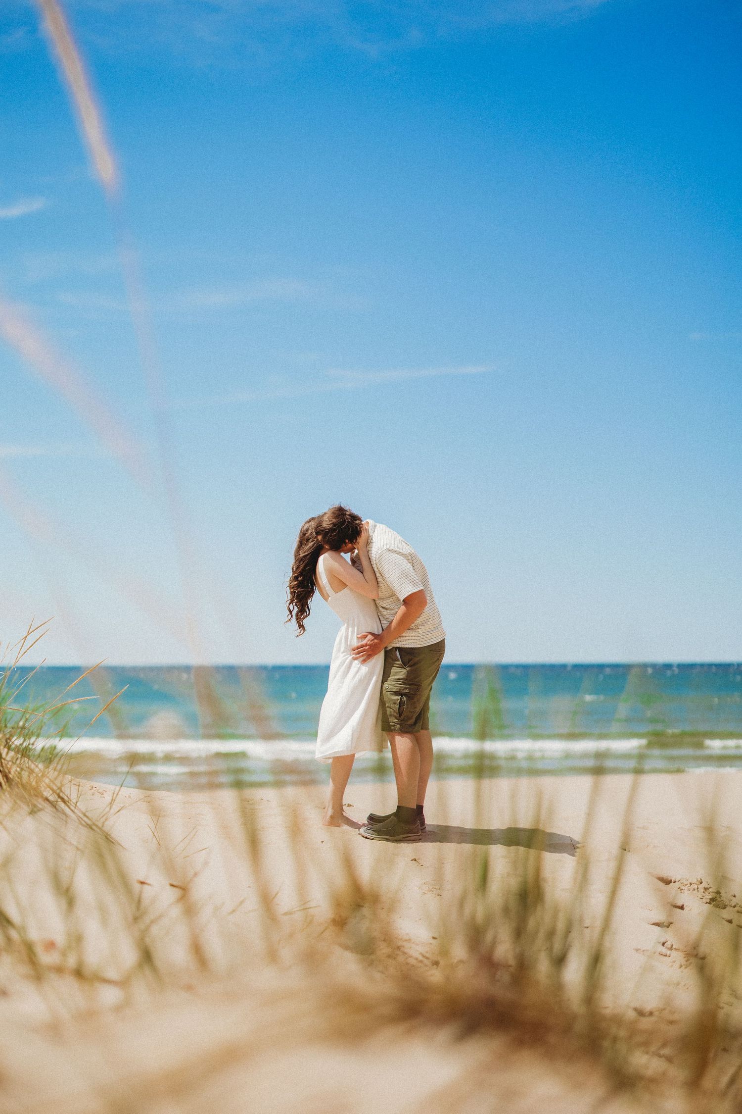 Dreamy beach scene with figures silhouetted against bright blue sky and sea grass.