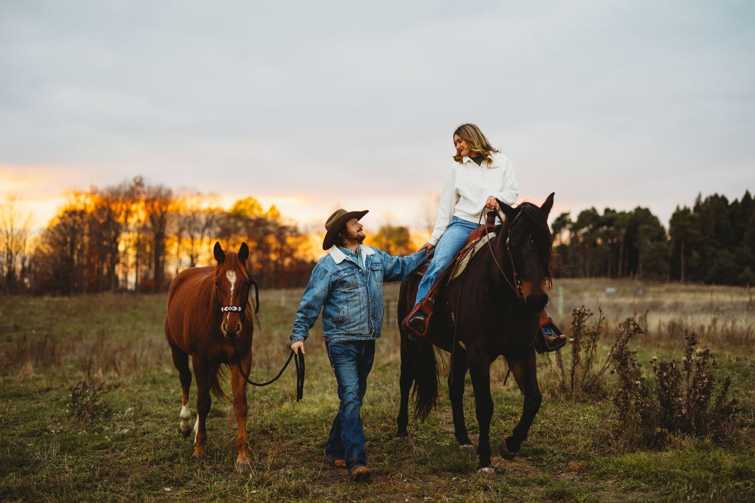 Silhouettes of people and horses against a sunset sky in an open field.